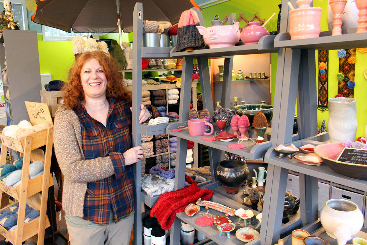Brinnon and Quilcene Community Knitters founder and Fiber and Clay owner Lise Solvang stands next to one of the shelves displaying knitted and clay creations at the store Thursday morning. (Zach Jablonski/Peninsula Daily News)                                Brinnon and Quilcene Community Knitters founder and Fiber and Clay owner Lise Solvang stands next to one of the shelves displaying knitted and clay creations at the store Thursday morning. (Zach Jablonski/Peninsula Daily News)