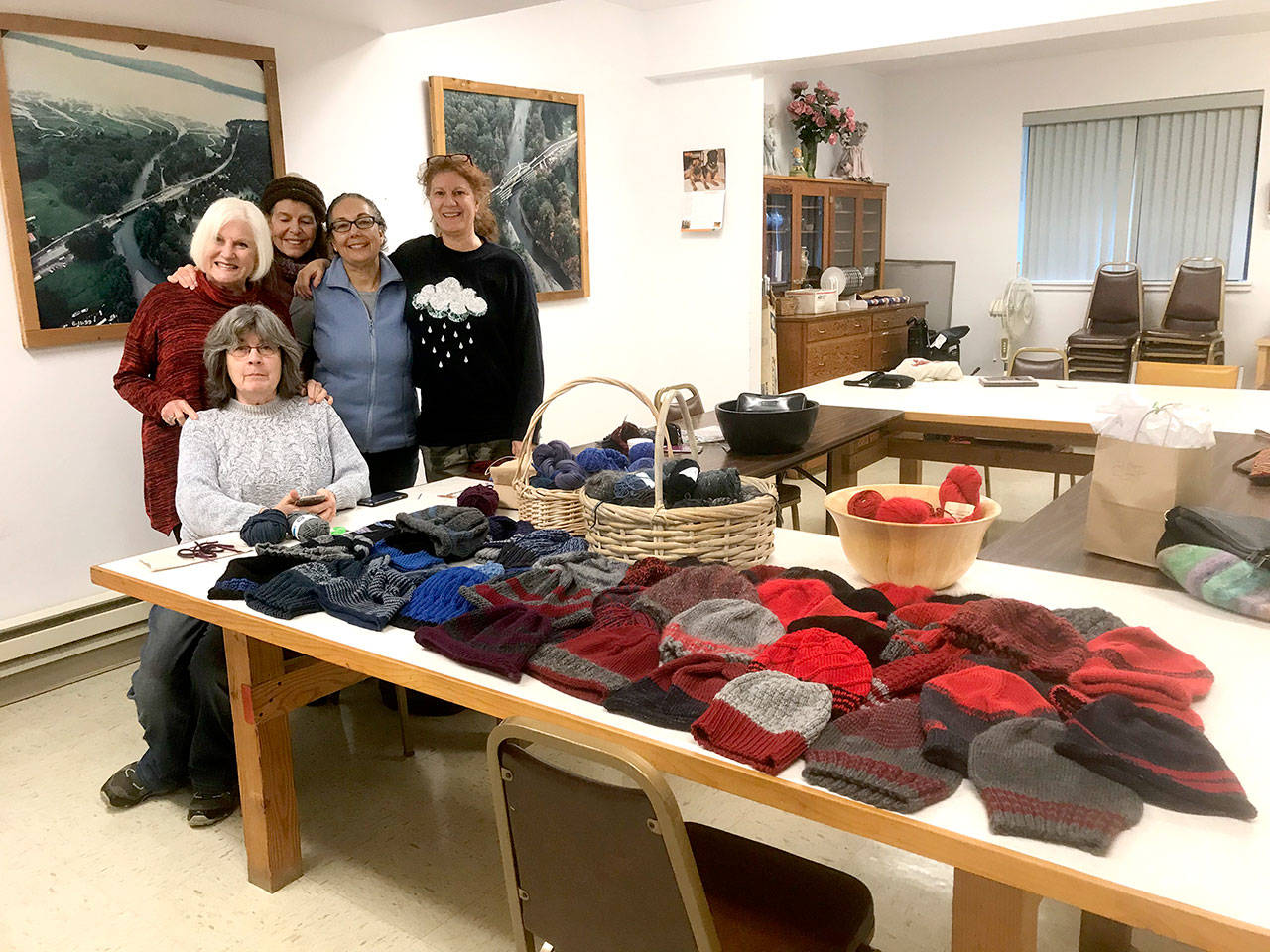 Brinnon and Quilcene Community Knitters members Pam Barnet, Nancy Nash, Cindy Germaine, Belinda Graham and Lise Solvang stand behind a table covered with hand-knit caps to be given to first responders at the Brinnon Community Center. (Brinnon and Quilcene Community Knitters)