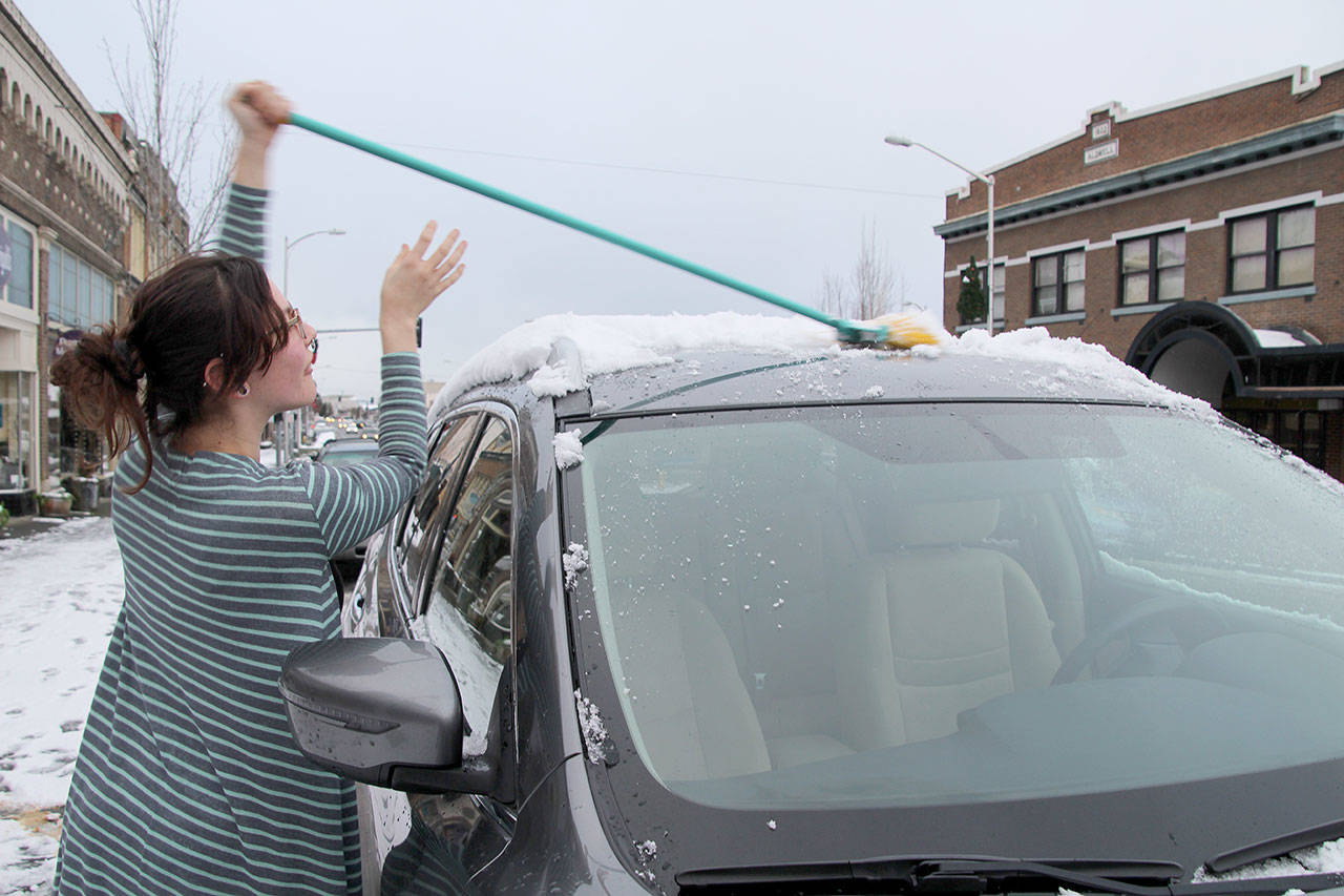 Alisha Stafford uses a broom to knock snow off a neighbor’s car outside Dr. Nivala’s Contact Lens and Eye Care Clinic on First Street. No one had a scraper, so she made use of the broom. (Maureen Heaster/Peninsula Daily News)