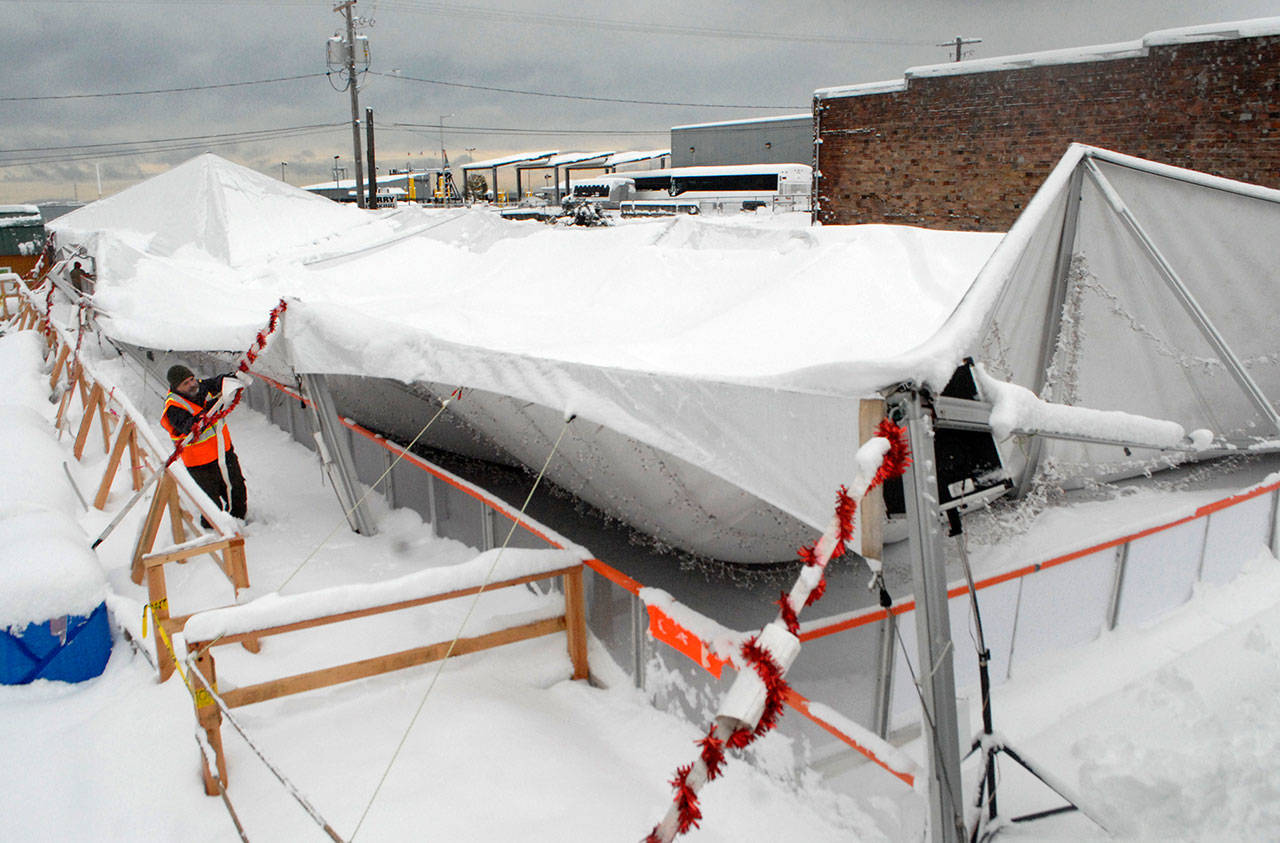 Steve Burke, a board member of the Port Angeles Regional Chamber of Commerce, releases tent straps that once supported the tent covering the ice rink at the Port Angeles Winter Ice Village on Wednesday morning after the tent collapsed overnight under the weight of up to 18 inches of snow. (Keith Thorpe/Peninsula Daily News)