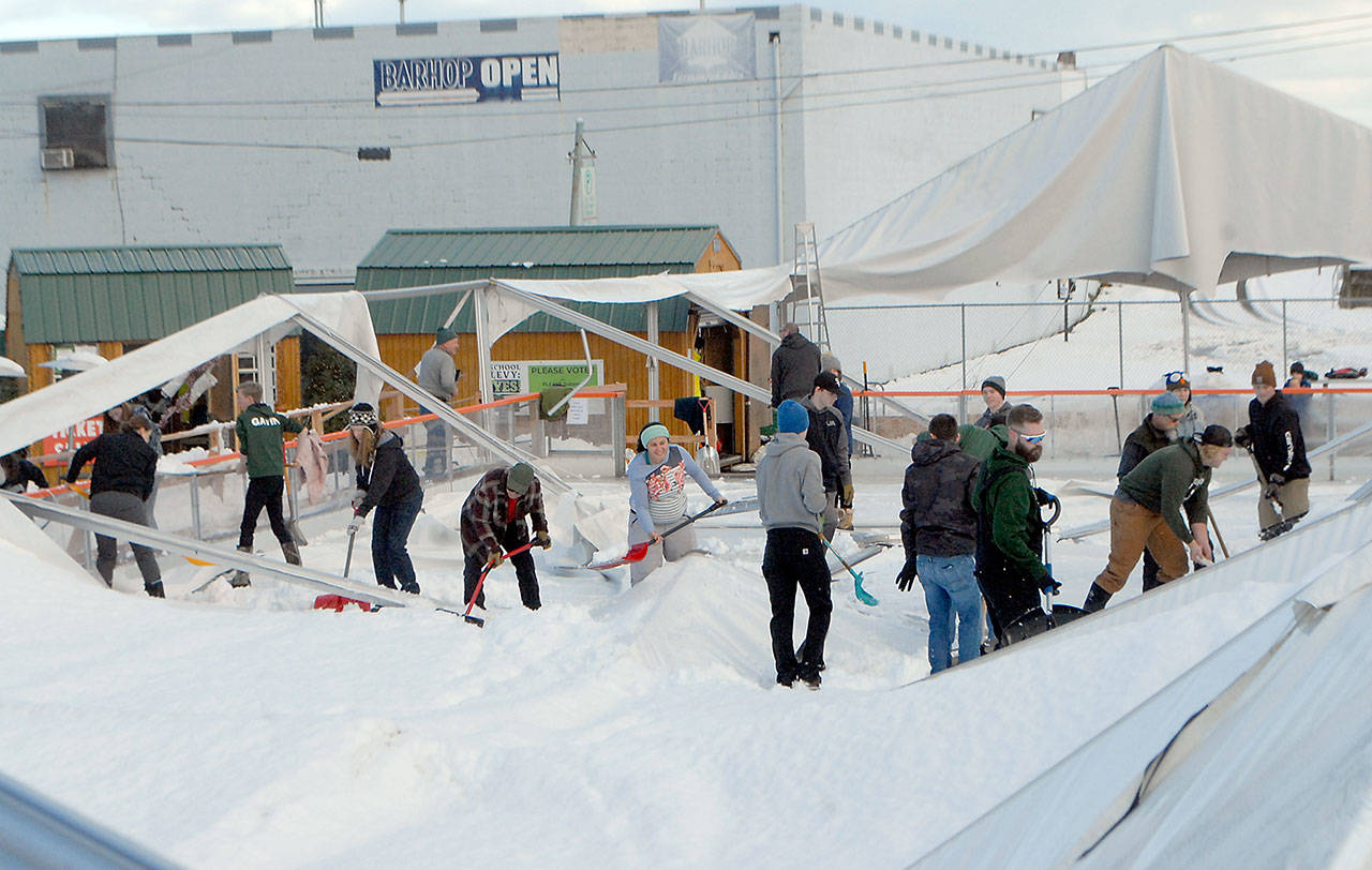 A collection of volunteers, including members of Port Angeles High School athletic teams, work to clear snow from the wreckage of the tent that covered the ice skating rink at the Port Angeles Ice Village on Thursday. The tent collapsed under the weight of heavy snow Wednesday morning. (Keith Thorpe/Peninsula Daily News)