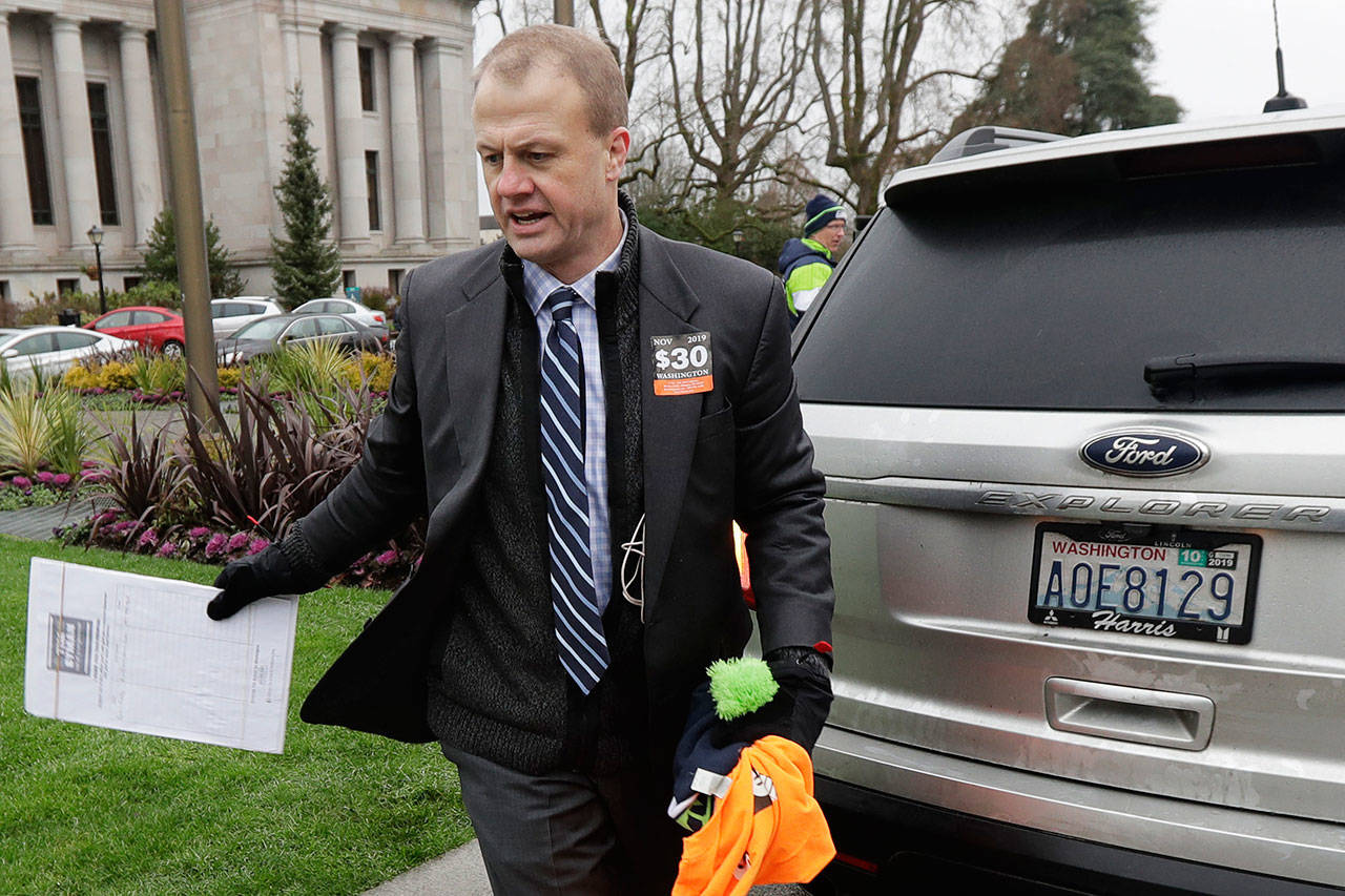 In this Jan. 13, 2020, photo, initiative activist Tim Eyman, who also is running as an independent for Washington governor, carries a clipboard as he walks next to his expired car registration tabs before attending a rally on the first day of the 2020 session of the Washington legislature at the Capitol in Olympia. (Ted S. Warren/The Associated Press)