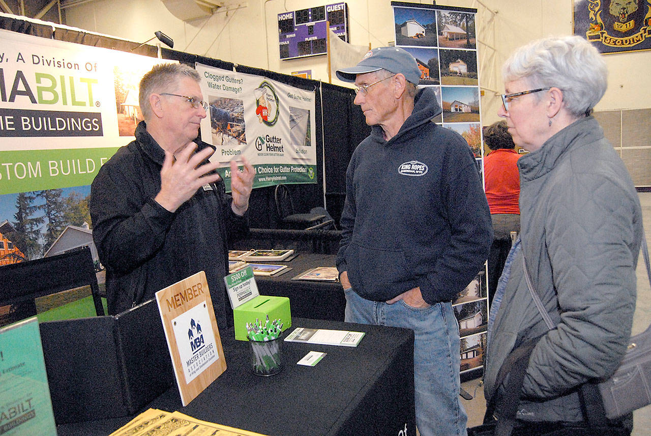 Will Johnson of Lynnwood-based PermaBilt Post Frame Buildings, left, speaks with Brad and Marla Varner of Sequim at his company’s booth during the 2019 Building, Remodeling and Energy Expo in the gymnasium of Sequim High School. (Keith Thorpe/Peninsula Daily News)