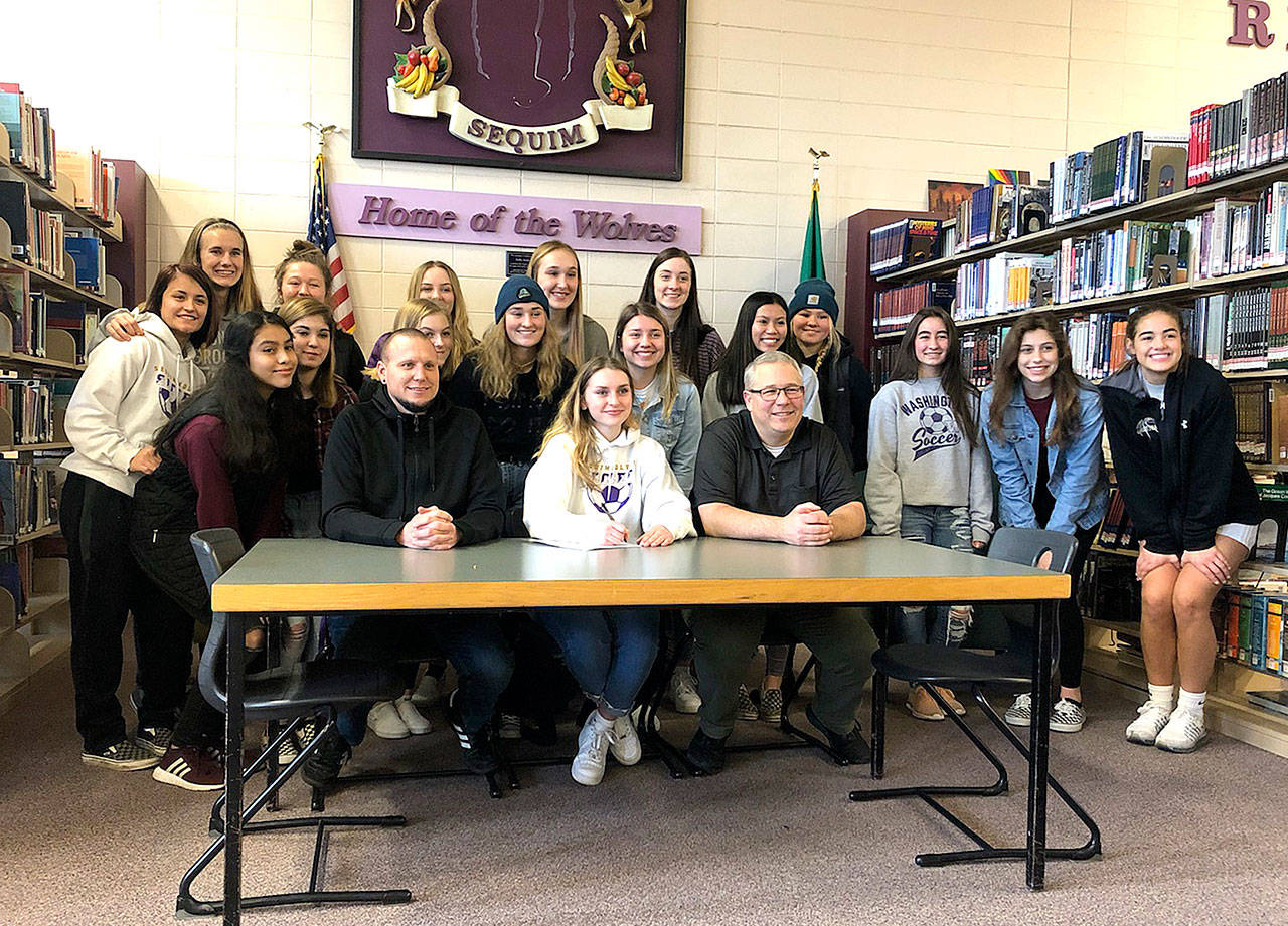 Sequim High School senior Gabrielle Happe, center in white, signs her letter of intent to play soccer at Edmonds Community College next year. Happe is joined by Sequim girls soccer head coach Derek Vandervelde, left center, Sequim athletic director Dave Ditlefsen, center right, and a number of her friends and soccer teammates. Happe will be joined at Edmonds by Port Angeles soccer player Lucah Folden.