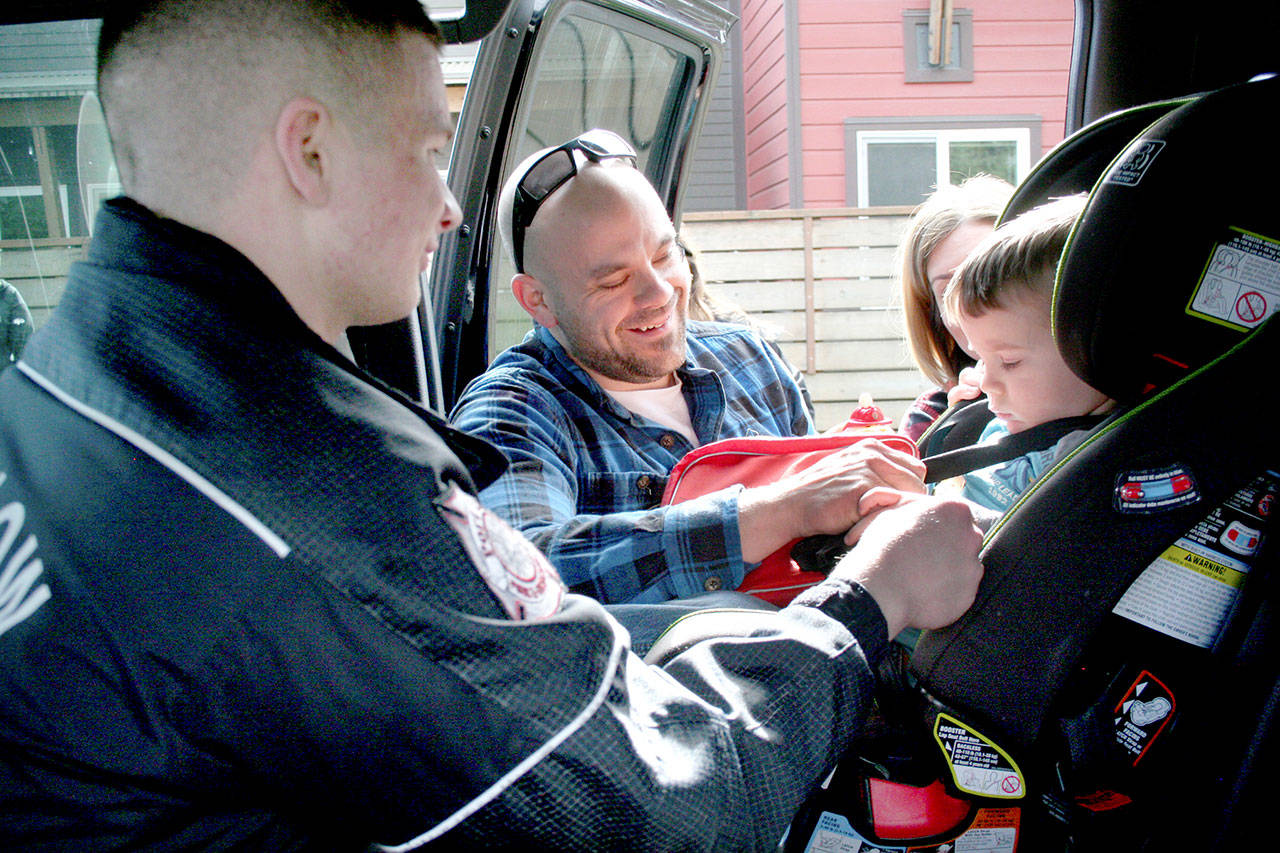 Port Ludlow Fire & Rescue firefighter Elliot Stone, left, helps Trevor Bergen load his son, Emmett, 2, into a car seat Thursday afternoon at the Chimacum Fire Station. (Brian McLean/Peninsula Daily News)
