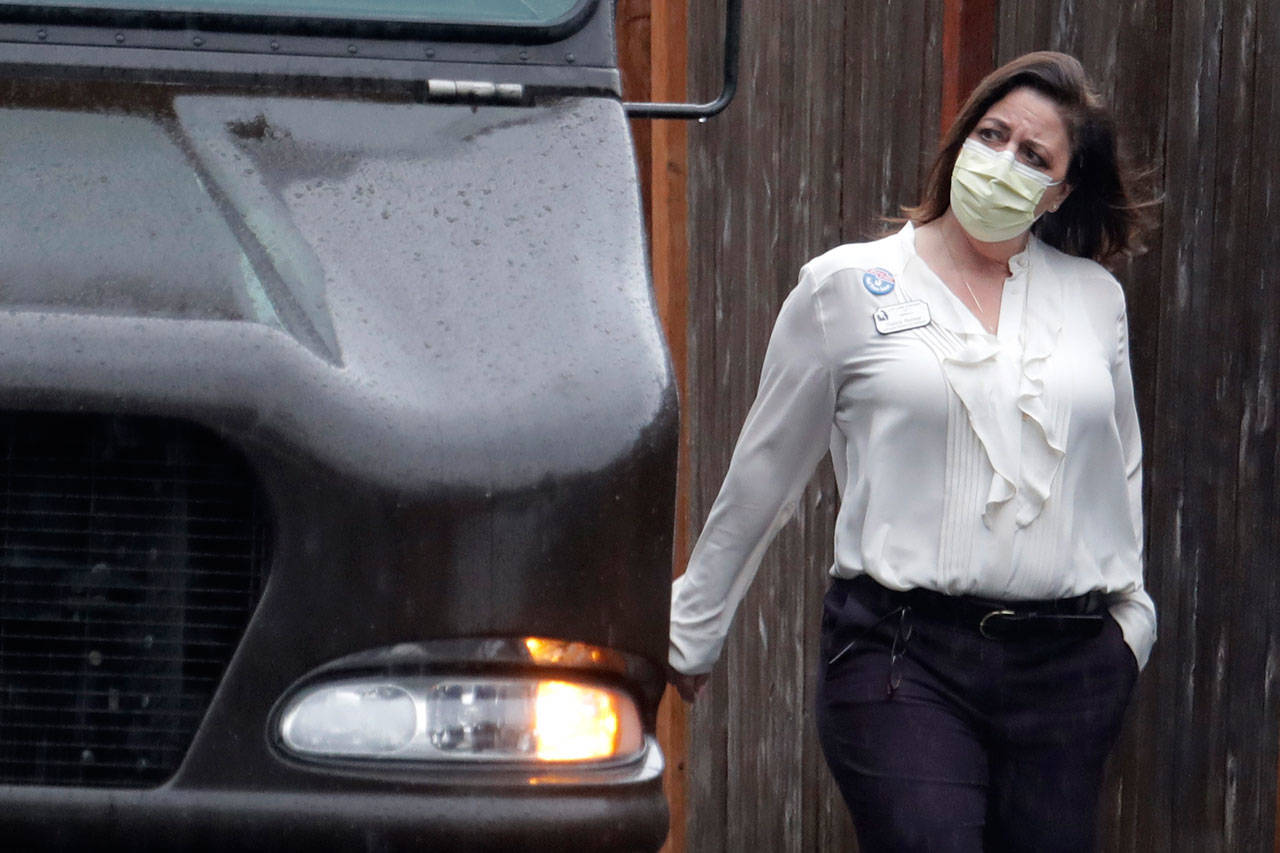 A worker at the Life Care Center in Kirkland, near Seattle, wears a mask as she walks near a UPS truck during a package delivery Monday, March 2, 2020. Several of the people who have died in Washington state from the COVID-19 coronavirus were tied to the long-term care facility, where dozens of residents were sick. (Ted S. Warren/The Associated Press)