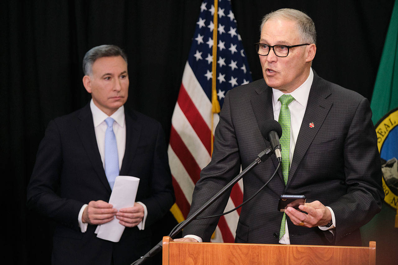 Washington Gov. Jay Inslee reads from an email from his mobile phone as he talks to reporters while King County Executive Dow Constantine listens Wednesday, March 11, 2020, during a news conference in Seattle. In efforts to slow the spread of the coronavirus, Inslee announced a ban on large public gatherings in three counties in the metro Seattle area. The vast majority of people recover from the new coronavirus. According to the World Health Organization, most people recover in about two to six weeks, depending on the severity of the illness. (Stephen Brashear/The Associated Press)
