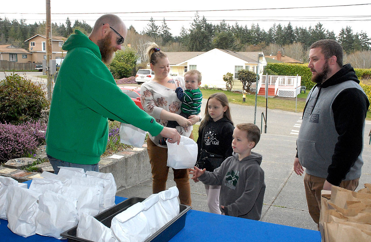 Thomas Fordham, a paraeducator at Franklin School in Port Angeles, left, passes out take-away lunch and breakfast bags to children of the McNeely family, from left, Brayden, 2, Misty, 7, and Jarrett, 6, as parent Stacy and Brady McNeely of Port Angeles watch on Tuesday in front of the school. (Keith Thorpe/Peninsula Daily News)