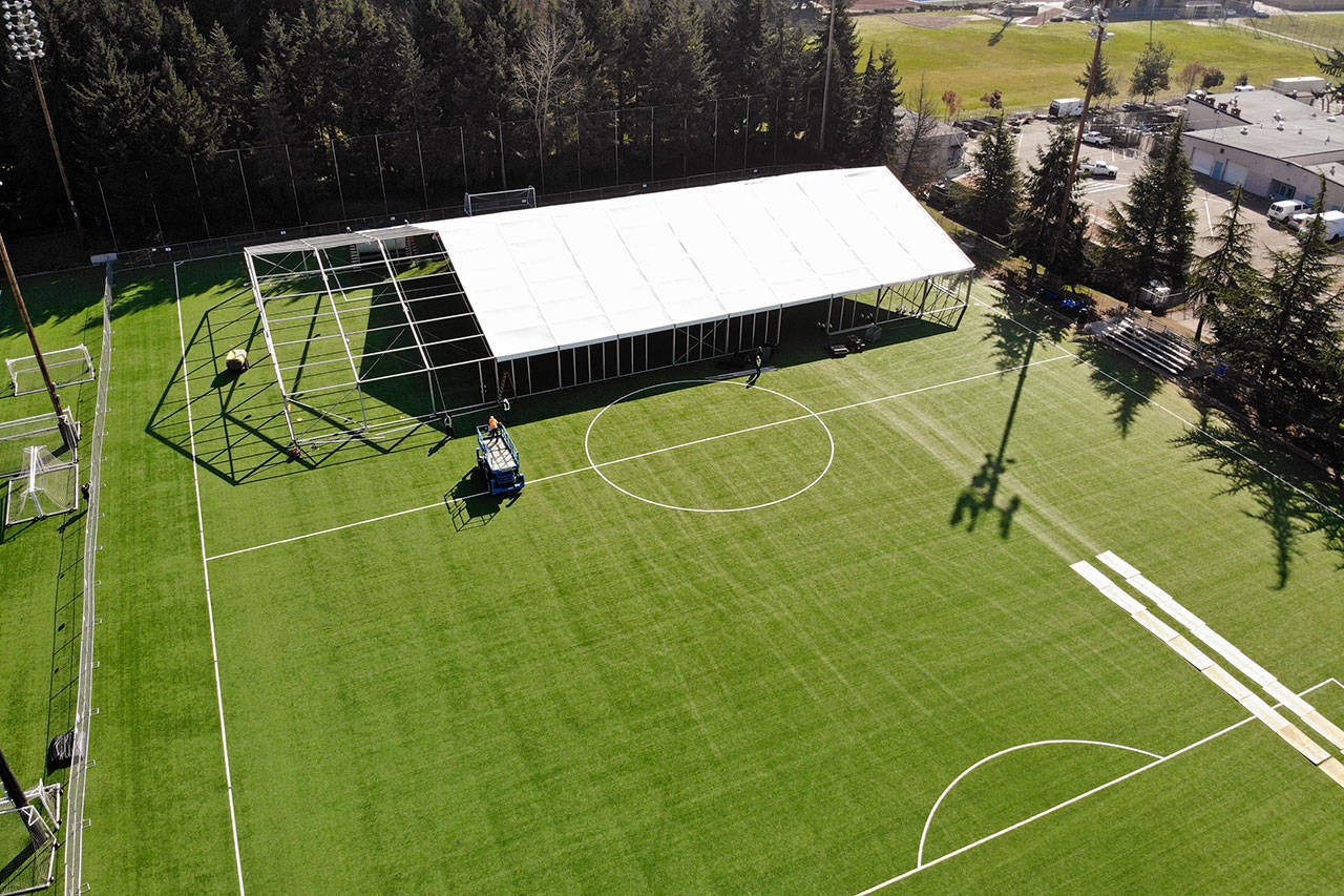 In this aerial drone photo, workers erect a temporary field hospital for use by people unable to isolate and recover from COVID-19 in their own homes on a soccer field Thursday, March 19, 2020, in the Seattle suburb of Shoreline. The field hospital will provide up to 200 beds, according to a city website, and will house “people exposed to, at risk of exposure, or becoming ill with the novel coronavirus.” (Elaine Thompson/The Associated Press)