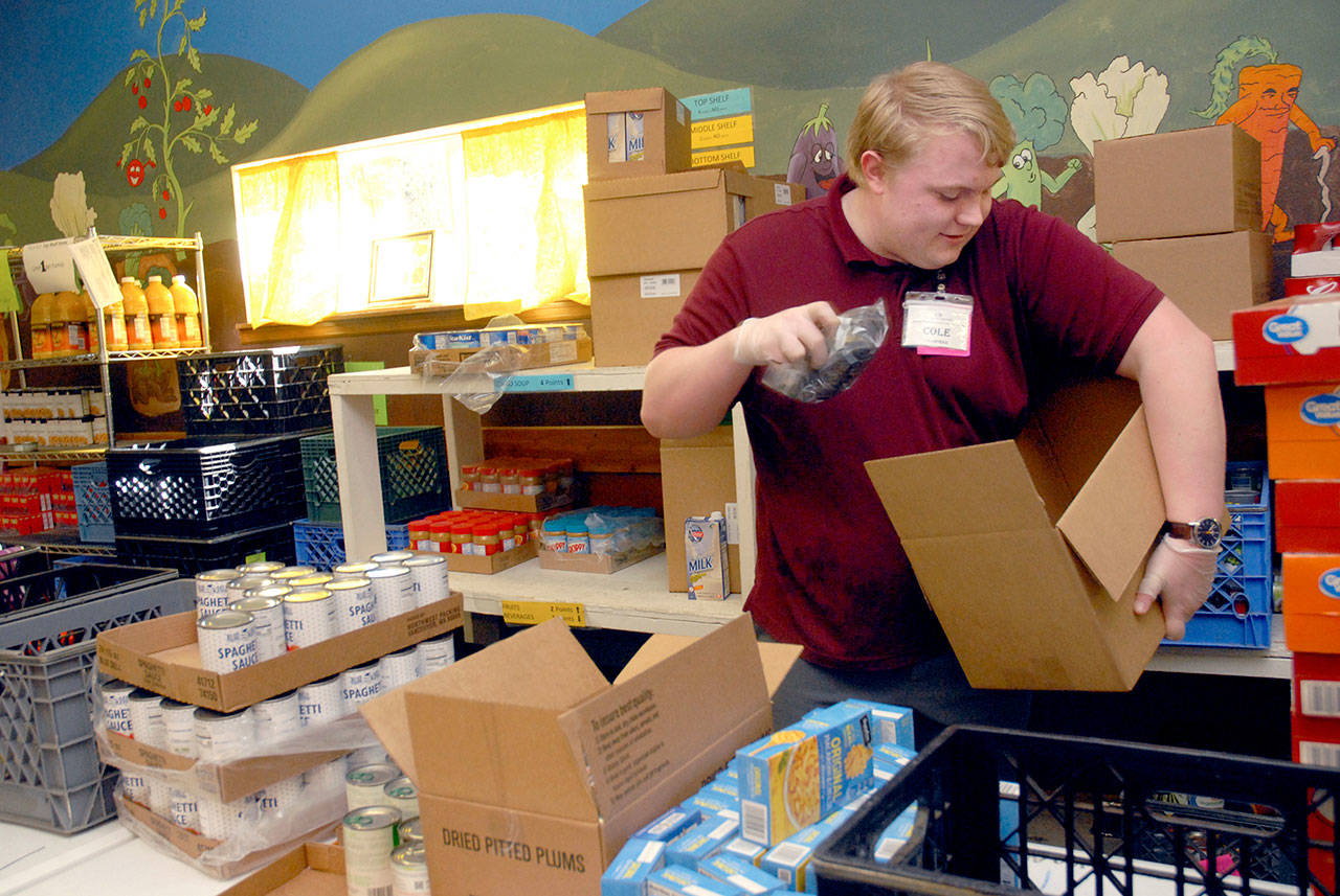 Keith Thorpe/Peninsula Daily News Volunteer Cole Wash fills a box with food and commodites for distribution to the public on Friday at the Port Angeles Food Bank.