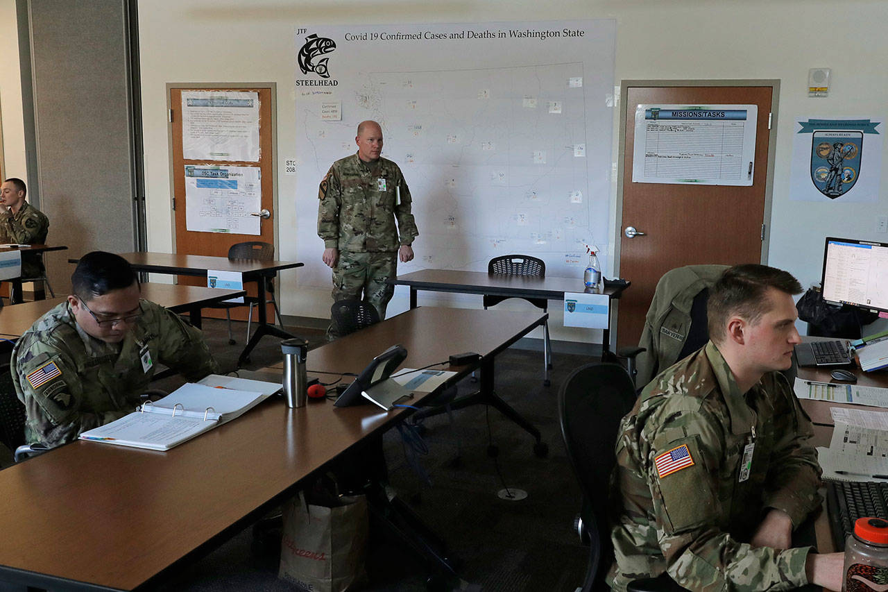 Washington Army National Guard Col. Kevin McMahan, center, stands next to a map of confirmed positive cases and deaths attributed to the new coronavirus in Washington state as he observes activities in the operations room for the coordination of Washington National Guard troops and active duty U.S. Army soldiers working in Washington state in response to the new coronavirus outbreak Tuesday, March 31, 2020, at Camp Murray, Wash. McMahan is the title 32 deputy commander with Joint Taskforce Steelhead, the coordinated effort between the Washington National Guard and a field hospital unit of U.S. Army soldiers from Colorado who are setting up a field hospital for non-coronavirus patients at the CenturyLink Field Events Center in Seattle. (Ted S. Warren/The Associated Press)