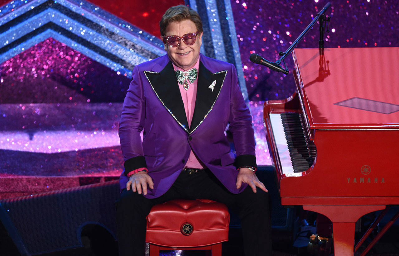 In this Sunday, Feb. 9, 2020, file photo, Elton John appears after performing his nominated song, “(I’m Gonna) Love Me Again,” at the Oscars in Los Angeles. The Elton John-led starry benefit concert that featured Billie Eilish, Mariah Carey and Alicia Keys on Sunday has raised nearly $8 million to battle the coronavirus. The musicians performed from their homes for the hour-long event that aired on Fox and iHeartMedia radio stations. The money will go to Feeding America and First Responders Children’s Foundation. (Chris Pizzello/Associated Press file)