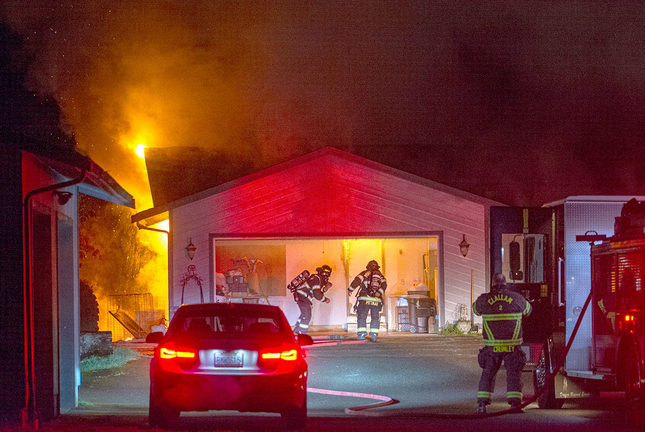 Firefighters from Clallam County Fire District No. 2 enter a burning house at 1802 S. Golf Course Road through its garage Thursday, April 2, 2020, in Port Angeles. (Jesse Major)