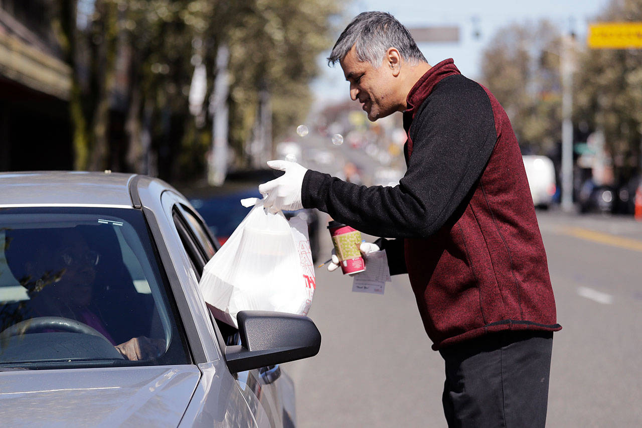 In this Tuesday, March 31, 2020, photo, Glen Quadros, owner of the Great American Diner & Bar, hands over a takeout food order, packaged in compostable containers placed inside a plastic bag, to a waiting customer in Seattle. Just weeks earlier, cities and even states across the U.S. were busy banning straws, limiting takeout containers and mandating that shoppers bring reusable bags or pay a small fee. Grocery clerks are nervous that the virus could linger on reusable fabric bags and their unions are backing them up with demands to end plastic bag fees and suspend bag bans. The plastics industry has seized the moment, lobbying to overturn existing bans on single-use plastics. (Elaine Thompson/The Associated Press)