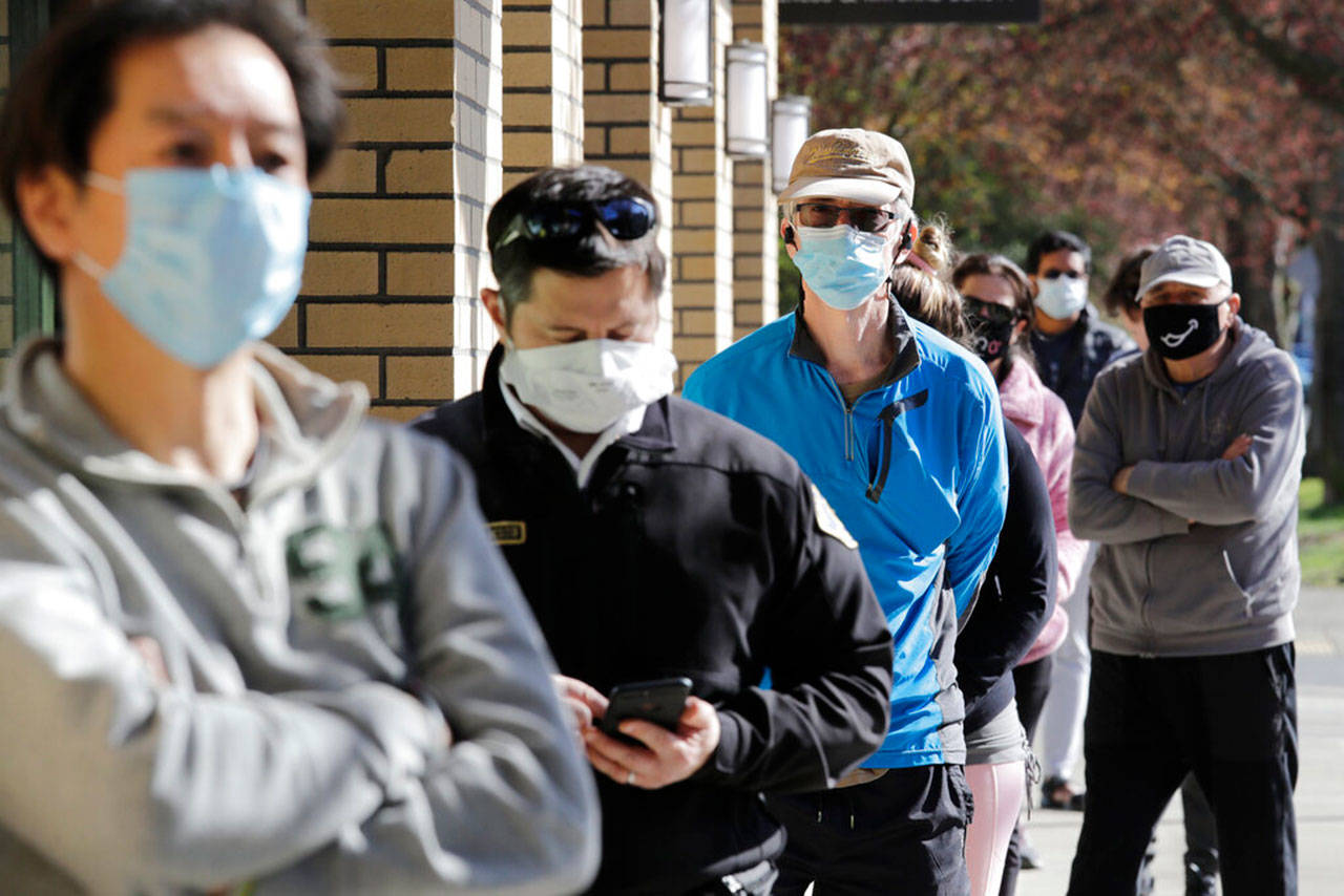 Customers wear a variety of protective masks as they wait some six-feet apart to enter a Trader Joe’s store, where the number of customers allowed inside at any one time was limited because of the coronavirus outbreak Wednesday, April 8, 2020, in Seattle. (Elaine Thompson/The Associated Press)