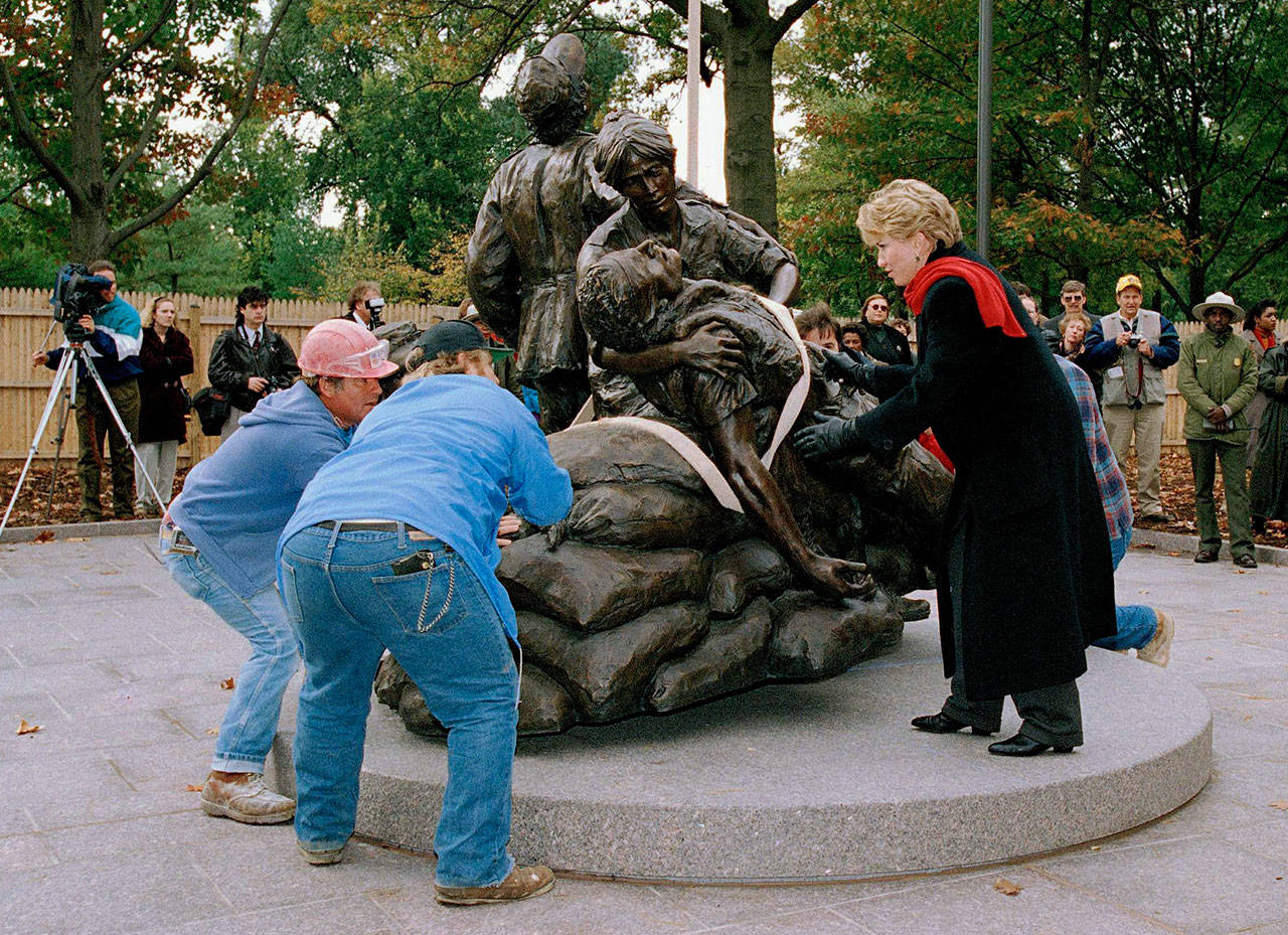 In this Nov. 1, 1993, file photo, sculptor Glenna Goodacre, right, helps workers guide the Vietnam Women’s Memorial into place in Washington. The bronze statue depicting three Vietnam era women and a wounded male soldier was placed near the Vietnam Veterans Memorial. Goodacre, 80, has died. Family members said Goodacre died of natural causes Monday night, April 13, 2020, at her Santa Fe, N.M., home. News of her death was posted to the Instagram page of Harry Connick Jr., who is married to her daughter, Jill. (AP Photo/Doug Mills, File)