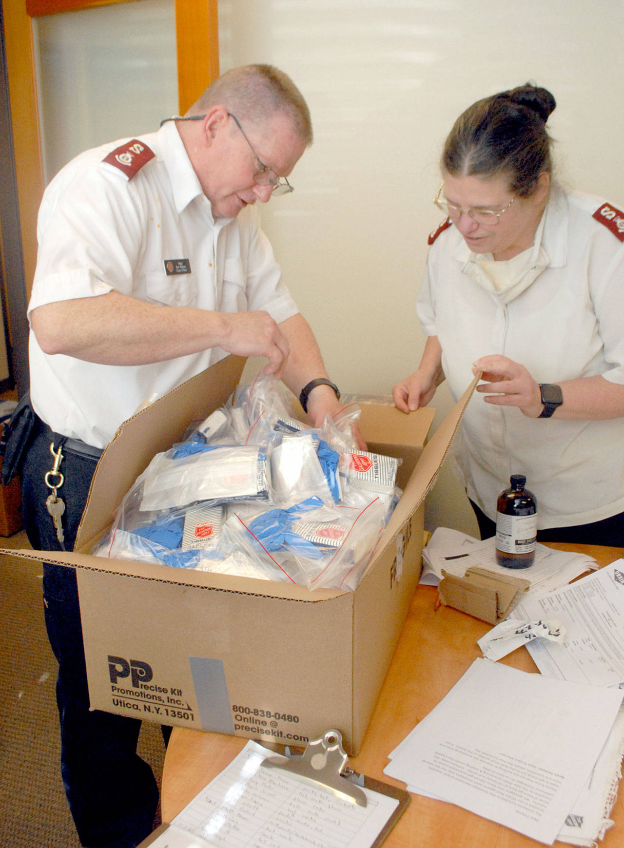 Port Angeles Salvation Army Majors Ron and Barbara Wehnau look over a box of self-protection packages that include soap, face masks and tissues packaged for distribution to the organization’s clients. (Keith Thorpe/Peninsula Daily News)