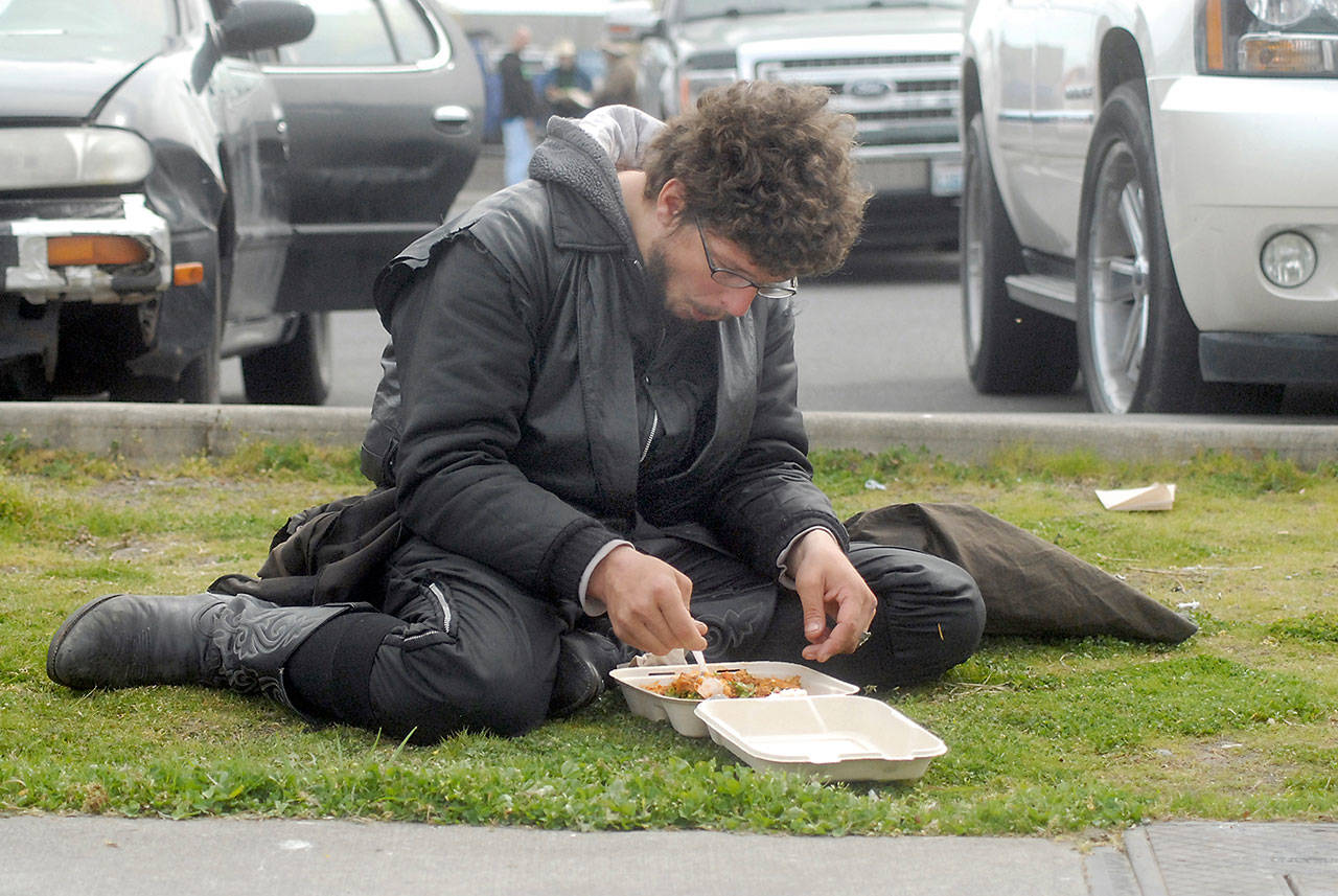 Kameron Madison, who said he was homeless, eats a carry-out meal next to the parking lot in front of the Port Angeles Salvation Army on Friday. (Keith Thorpe/Peninsula Daily News)