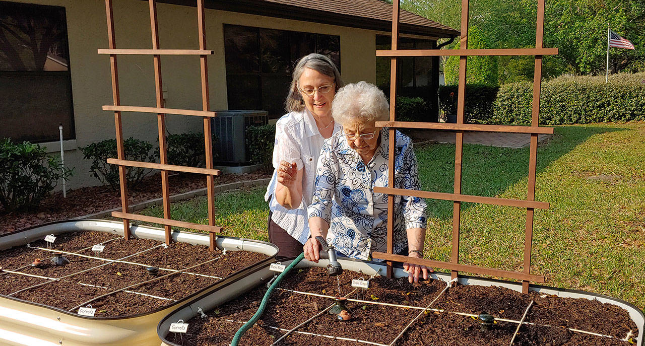 In this April 12, 2020, photo, Brenda Flowers, left, and 96-year-old Lorraine Tyree, water their plants in Crystal River, Fla. Backyard gardeners are coming together, mostly virtually, to learn and share stories on how to grow vegetables, fruits and flowers as the novel coronavirus raises fears about disruptions in food supplies and the cost of food in a down economy. (Ed Flowers via AP)