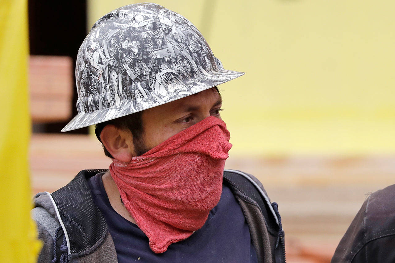A worker wears a cloth tied around his face as a makeshift mask on a townhouse construction site Friday, April 24, 2020, in Seattle. Gov. Jay Inslee announced that some construction projects will be allowed to resume amid the coronavirus pandemic, including “low-risk” projects and only with physical distancing and other requirements. (Elaine Thompson/Associated Press)