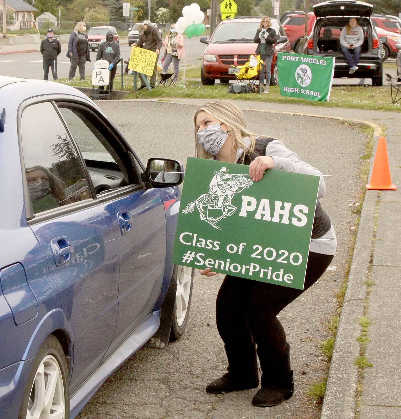 Nikki Brown, the mother of Port Angeles High School senior class President Logan Brown, gives a sign the parents helped create to a senior driving by in a vehicle Monday, May 4, 2020. (Dave Logan/for Peninsula Daily News)