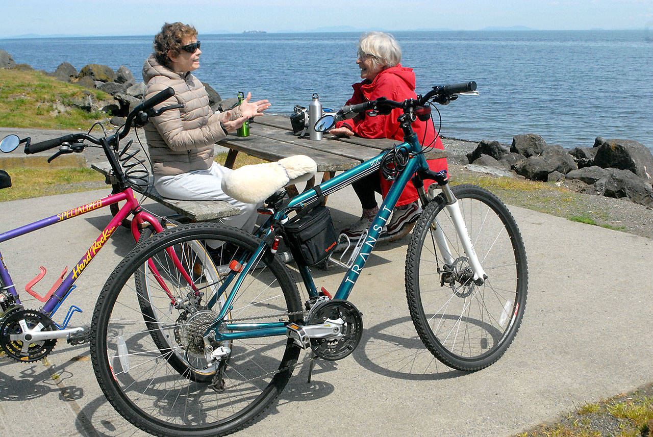 Bicycling friends Judith Parker, left, and Penney Van Vleet, both of Sequim, sit at a picnic table on the shore of Sequim Bay at Marlyn Nelson County Park at Port Williams near Sequim after the park was reopened by Clallam County on Tuesday, May 5, 2020. (Keith Thorpe/Peninsula Daily News)