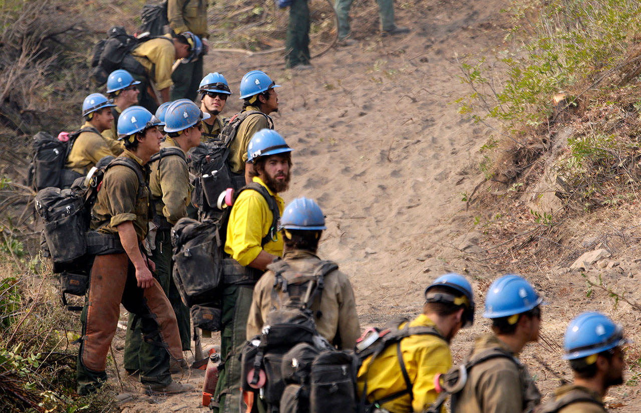 In this Aug. 27, 2015, file photo firefighters from the University of Alaska (Fairbanks) watch as a wildfire slowly creeps toward their fire break near Chelan, Wash. Newly released national plans for fighting wildfires during the coronavirus pandemic are hundreds of pages long but don’t offer many details on how fire managers will get access to COVID-19 tests or exactly who will decide when a crew needs to enter quarantine. (Elaine Thompson/Associated Press file)