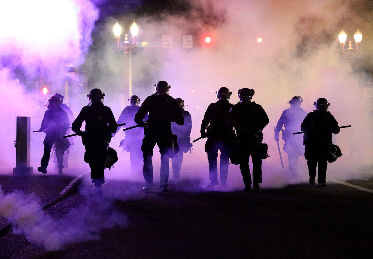 Police officers walk enveloped by teargas in Portland, Friday, March 29, 2020. After hours of largely peaceful demonstrations, violence escalated late Friday in downtown Portland, as hundreds of people gathered to protest the Minneapolis police killing of a black man, George Floyd. (Dave Killen/The Oregonian via AP)