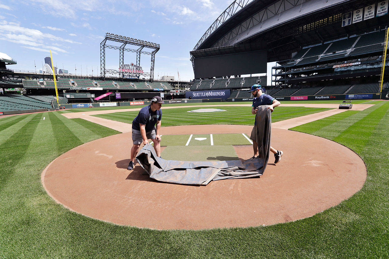 Grounds crew workers Jacob Weiderstrom, left, and Marcus Gignac pull a tarp off home plate as they continue to keep the Seattle Mariners’ field in playing shape as the ballpark goes into its seventh week without baseball played because of the coronavirus outbreak Monday, May 11, 2020, in Seattle. A person familiar with the decision tells The Associated Press that Major League Baseball owners have given the go-ahead to making a proposal to the players’ union that could lead to the coronavirus-delayed season starting around the Fourth of July weekend in ballparks without fans. (AP Photo/Elaine Thompson)