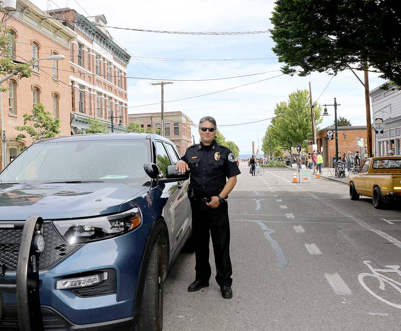 Port Townsend interim Police Chief Troy Surber stands with his patrol car while he prepares to help escort the Juneteenth march down Water Street last Friday. (Ken Park/Peninsula Daily News)
