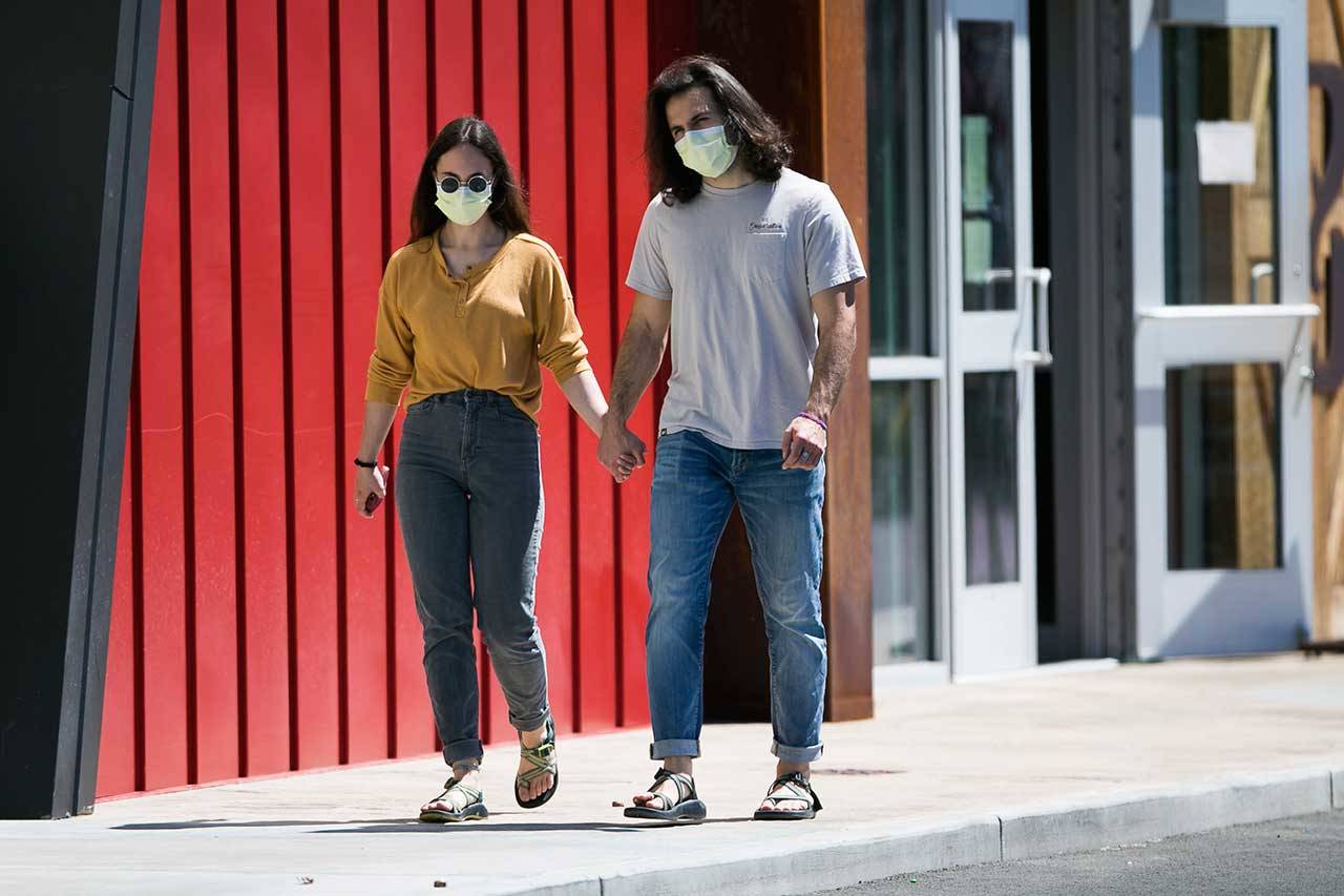 Hana Morris, left, and Forrest Golic wear masks as they walk hand-in-hand Monday in Yakima. Washington state will require people to wear facial coverings in most indoor and outdoor public settings under a statewide public health order announced Tuesday by Gov. Jay Inslee in response to ongoing COVID-related health concerns. Yakima County, which has been among the hardest hit by the outbreak, has even more stringent requirements under a separate proclamation issued by Inslee that also takes effect Friday. (Amanda Ray/Yakima Herald-Republic via AP)