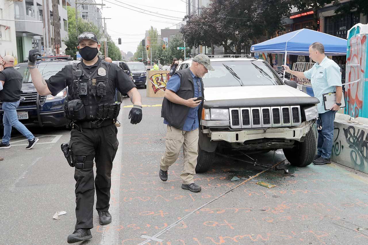 A Seattle police officer asks people to move aside to allow police vehicles through as investigators, right, look over a car involved in a shooting Monday in Seattle, where streets are blocked off in what has been named the Capitol Hill Occupied Protest zone. (Elaine Thompson/The Associated Press)