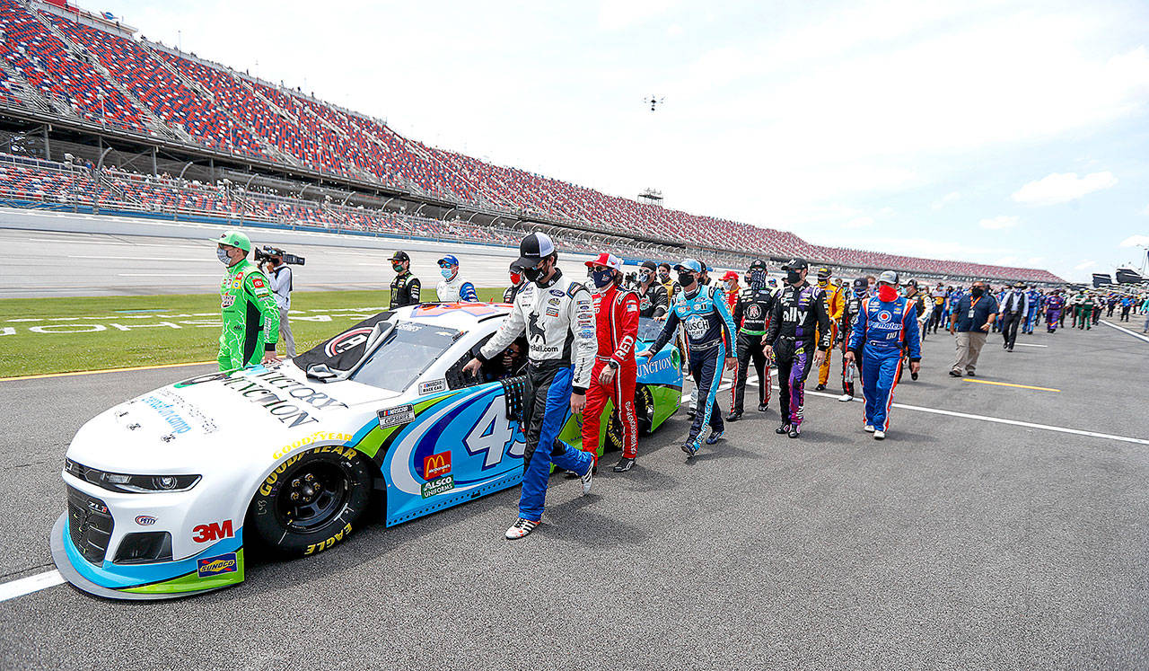 In this Monday June 22, 2020, file photo, NASCAR drivers Kyle Busch, left, and Corey LaJoie, right, join other drivers and crews as they push the car of Bubba Wallace to the front of the field prior to the start of the NASCAR Cup Series auto race at the Talladega Superspeedway in Talladega Ala. On Friday, June 26, 2020, The Associated Press reported on stories circulating online incorrectly asserting NASCAR allows a Black Lives Matter-themed car, but won’t allow its audience to wear MAGA hats or other Trump clothing. The auto racing association has not banned Trump-themed clothing, according to NASCAR spokesman Mike Forde. (John Bazemore/Associated Press)