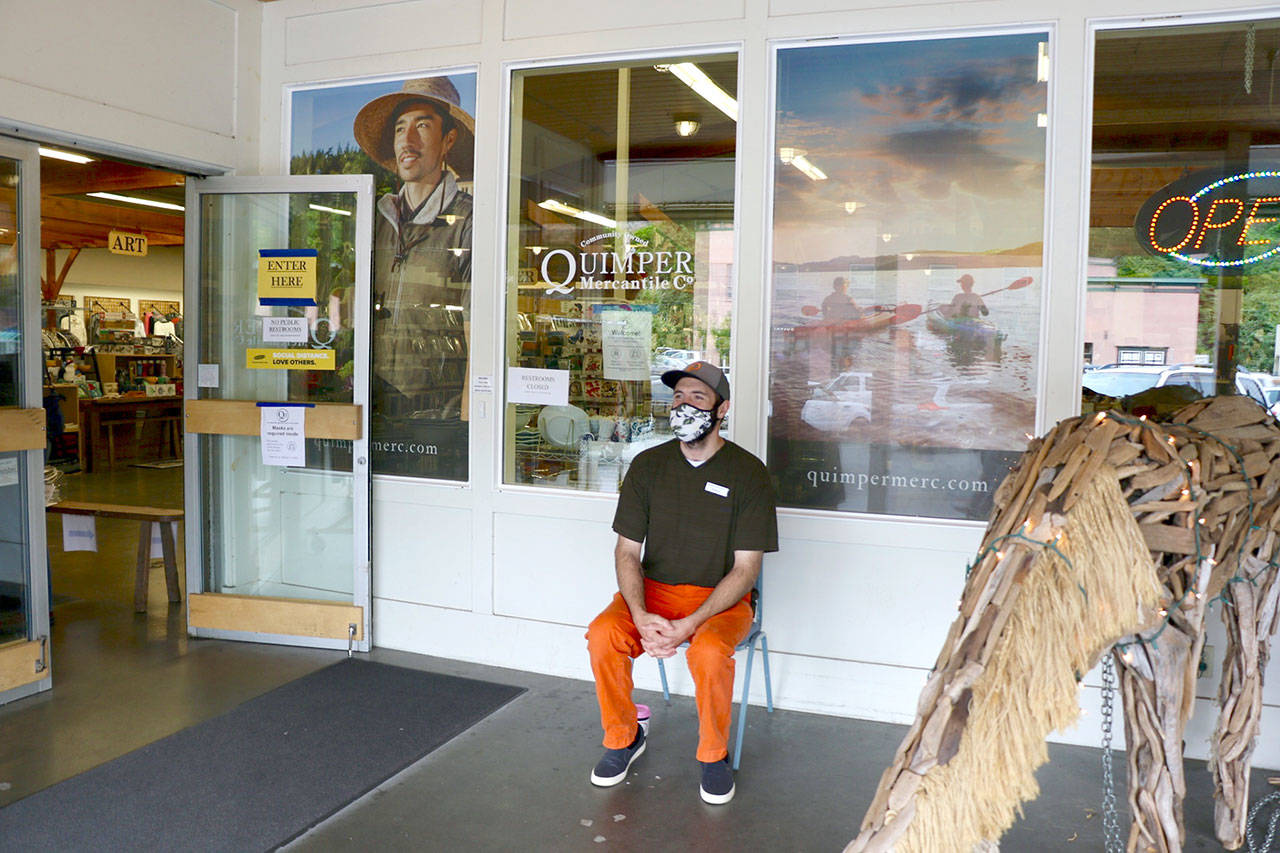A Quimper Mercantile employee sits outside the shop to act as a greeter and encourage customers to wear masks and use hand sanitizer. (Ken Park/Peninsula Daily News)