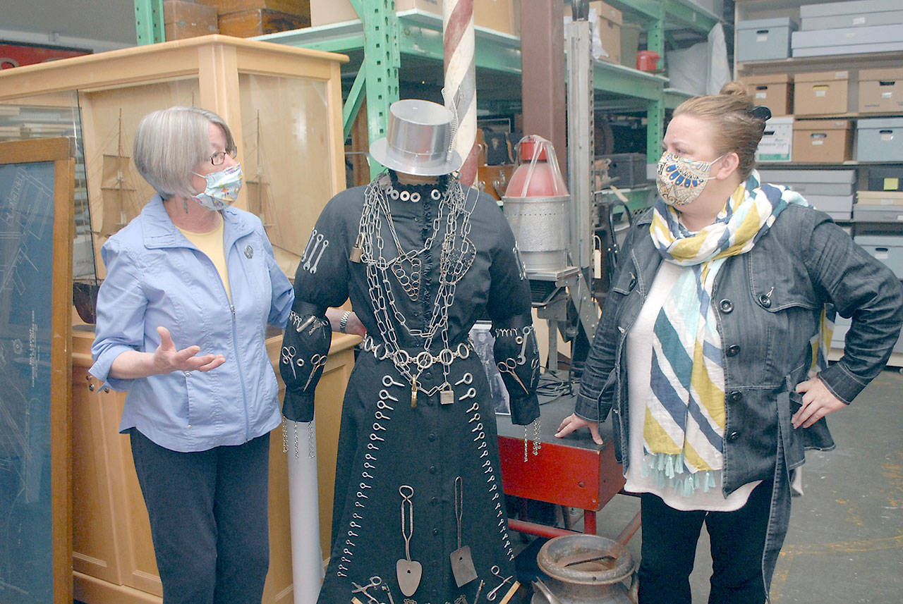 Kathy Estes, retiring executive director of the North Olympic History Center, formerly the Clallam County Historical Society, left, speaks with Amy McIntyre, who will begin work in that position in August. The pair discuss a mannequin adorned in a reproduction of an outfit made for a former downtown Port Angeles hardware store. (Keith Thorpe/Peninsula Daily News)