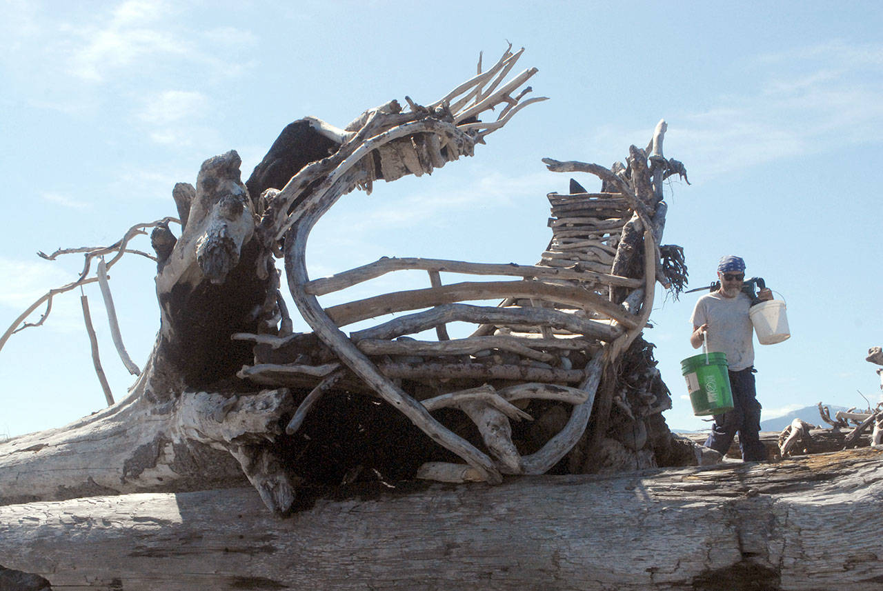 Sculptor Sky Darwin of Port Angeles deploys his tools Sunday, July 19, 2020, to reconstruct the driftwood heart on Ediz Hook. (Keith Thorpe/Peninsula Daily News)