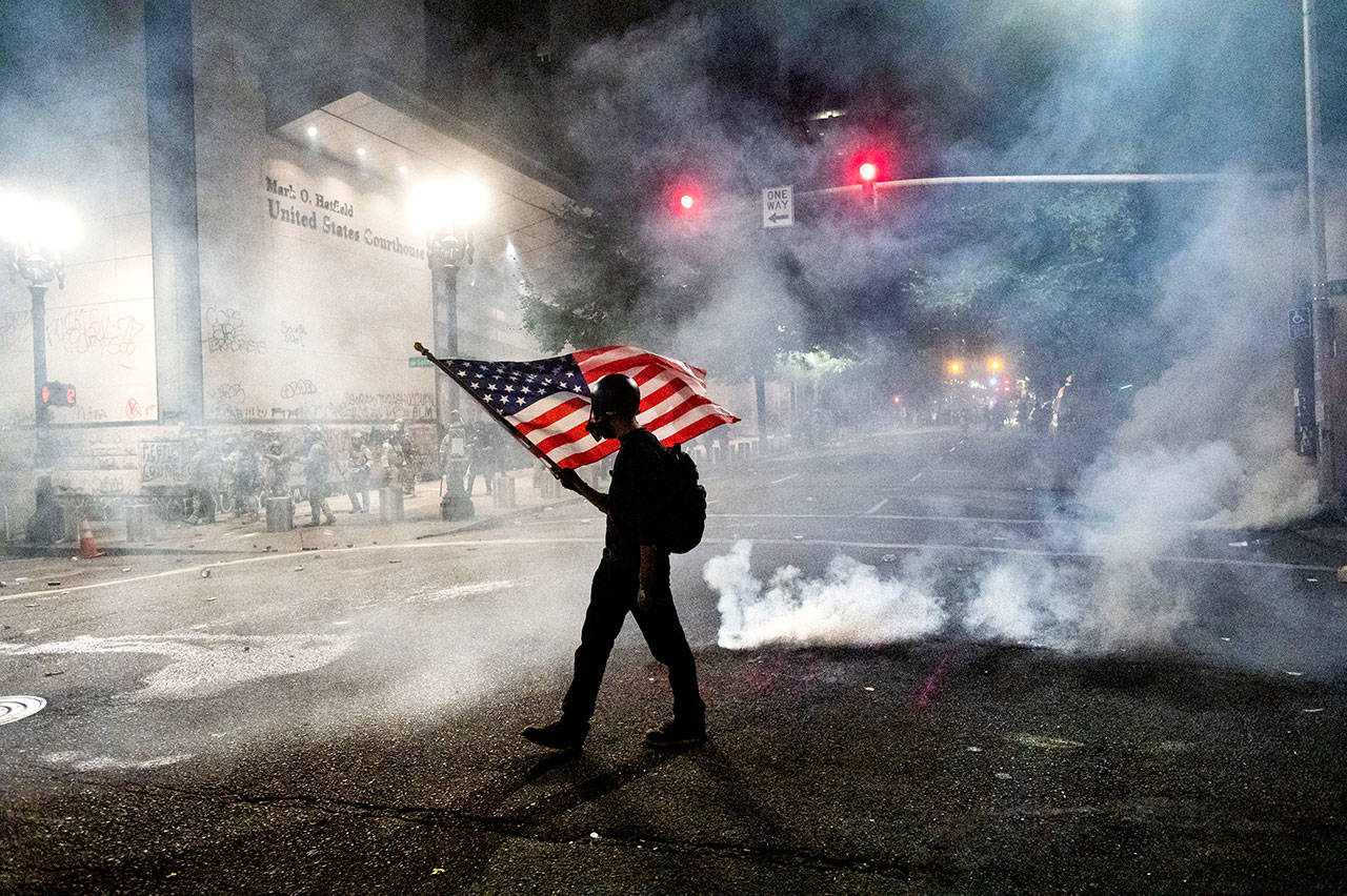 A Black Lives Matter protester carries an American flag as teargas fills the air outside the Mark O. Hatfield United States Courthouse on Tuesday, July 21, 2020, in Portland, Ore. (Noah Berger/Associated Press)