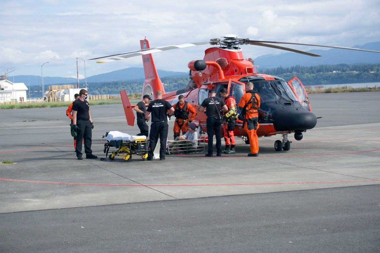 A Coast Guard Air Station Port Angeles MH-65 Dolphin rescue helicopter crew transfers an injured hiker’s care to emergency medical personnel at the air station in Port Angeles on Monday, Aug. 3, 2020, after the aircrew hoisted the hiker from Olympic National Park. The 17-year-old man fell and sustained knee and head injuries that required immediate medical attention. (Photo courtesy of U.S. Coast Guard)