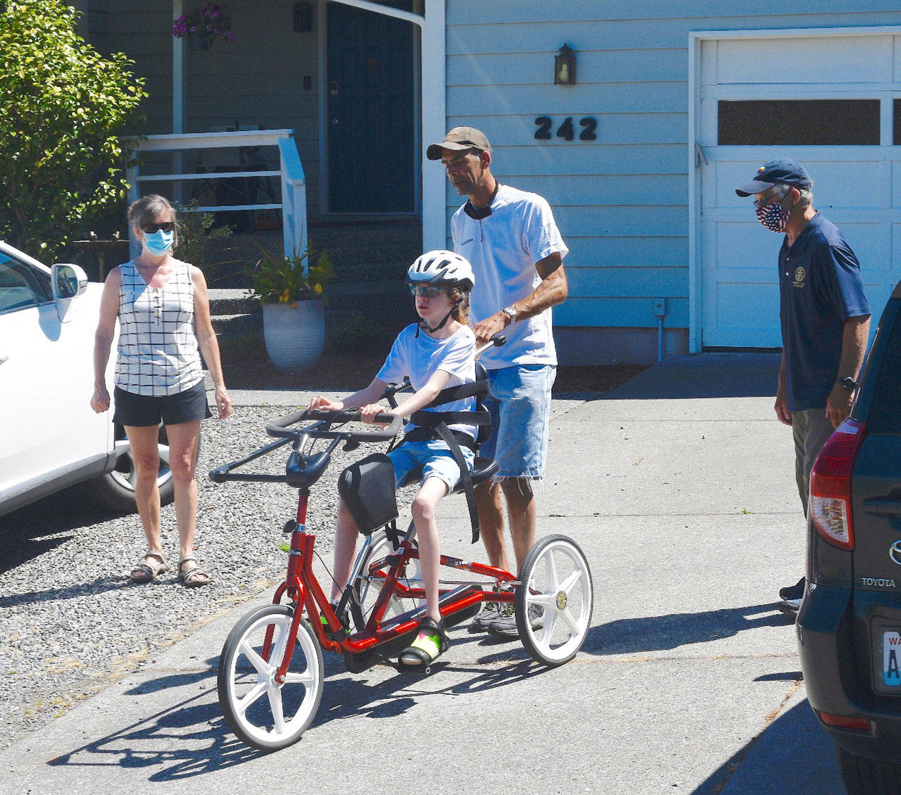 With Cherry Bibler, Sequim School District physical therapist, left, and Sequim Noon Rotary member Bob Macaulay, right, looking on, 11-year-old Abby Johnson takes a rides on her adaptive bike — with new steering bar — with help from her father, Alvin Pitts. (Photo by Doug Schwarz)