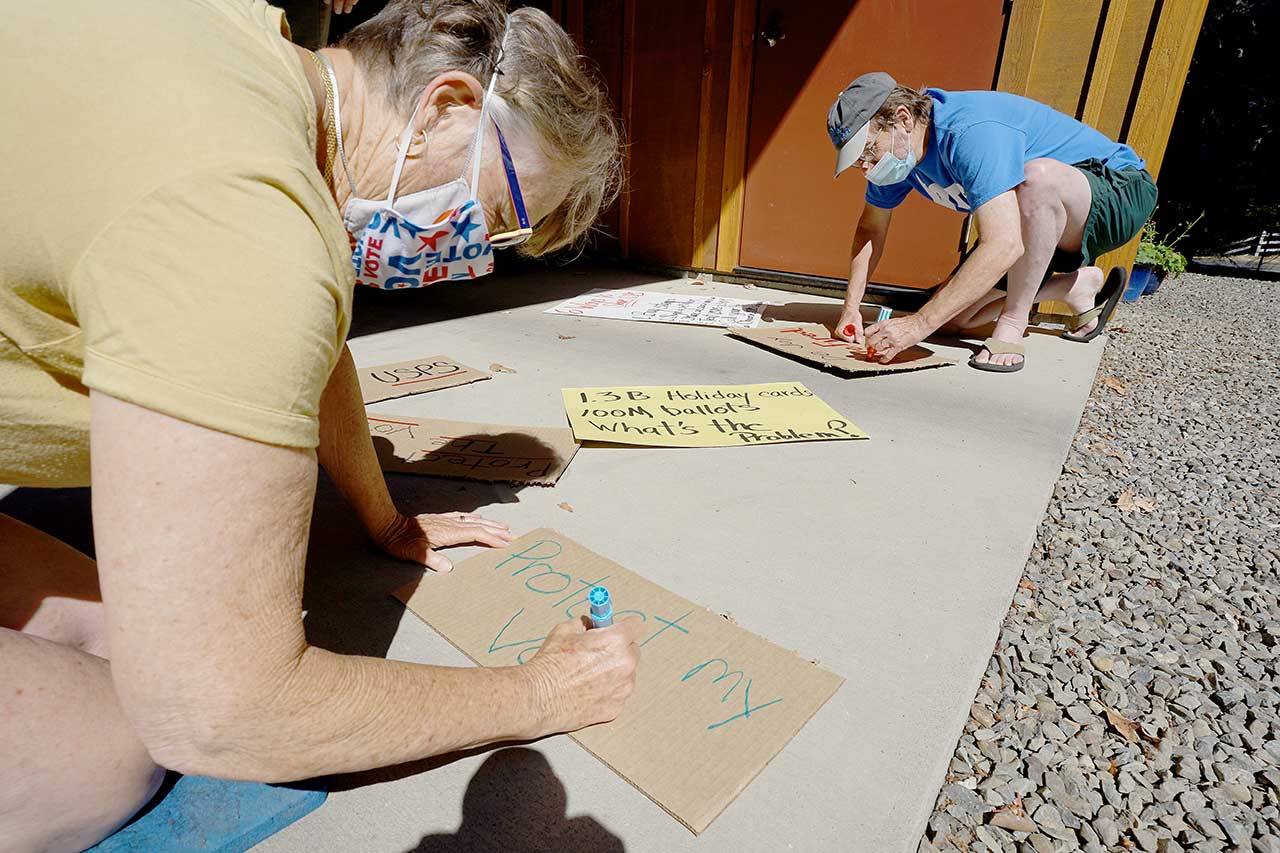 Debbi Steele, left, and Bruce Cowan make signs Monday, Aug. 17, 2020, in Steele’s driveway in Port Townsend ahead of a Tuesday rally in support of the U.S. Postal Service and its role in facilitating mail-in voting during the first presidential election to be held during a global pandemic. (Nicholas Johnson/Peninsula Daily News)
