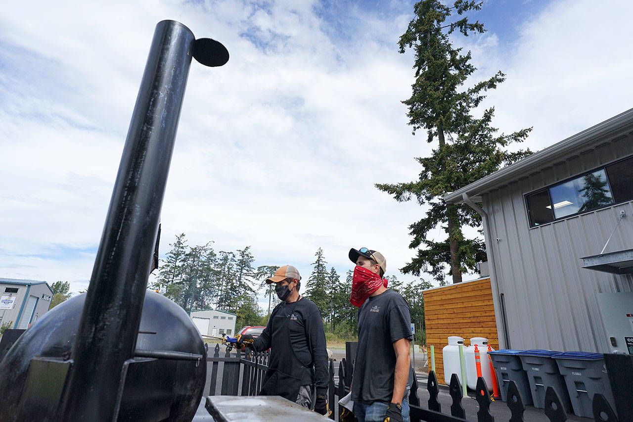 Mike Harbin of Mo-Chilli BBQ shows apprentice pitmaster Cody Taylor how to properly clean a smoker Thursday outside Lila’s Kitchen in Port Townsend. (Nicholas Johnson/Peninsula Daily News)