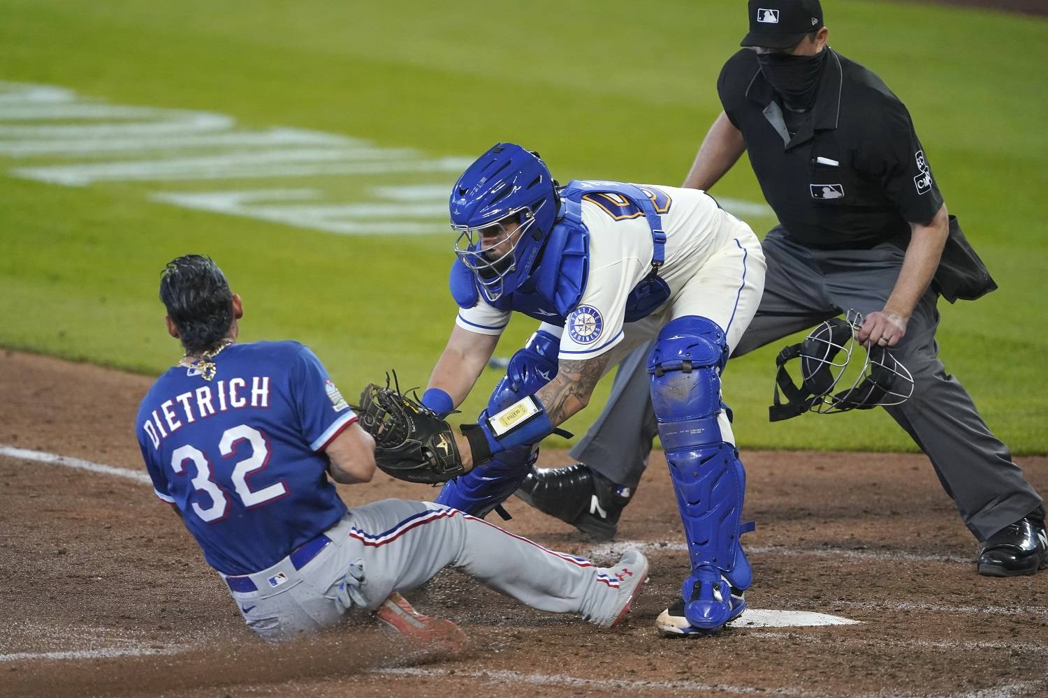Seattle Mariners catcher Joseph Odom tags out Texas Rangers’ Derek Dietrich as home plate umpire Lance Barrett looks on during the seventh inning Sunday in Seattle. Dietrich was trying to score on a double hit by Leody Taveras. (Ted S. Warren/The Associated Press)