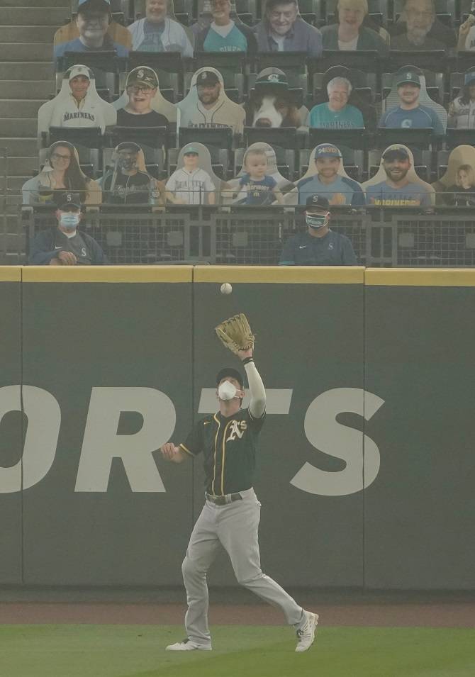 Oakland Athletics right fielder Stephen Piscotty, right, wears a mask as he catches a fly ball hit by Seattle Mariners’ Kyle Seager as smoke from wildfires fills the air at T-Mobile Park during the first inning of a doubleheader Monday in Seattle. (Ted S. Warren/Associated Press)