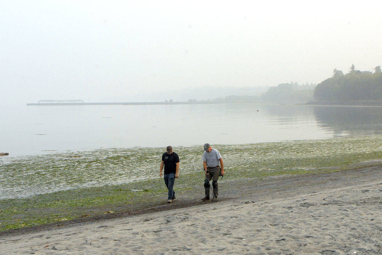 Johnathan Dewey of Sequim, left, accompanies Dane Petersen of Fortuna, Calif., as he uses a metal detector at Hollywood Beach in Port Angeles while a layer of smoke and haze lies over Port Angeles Harbor on Wednesday, Sept. 16, 2020. (Keith Thorpe/Peninsula Daily News)