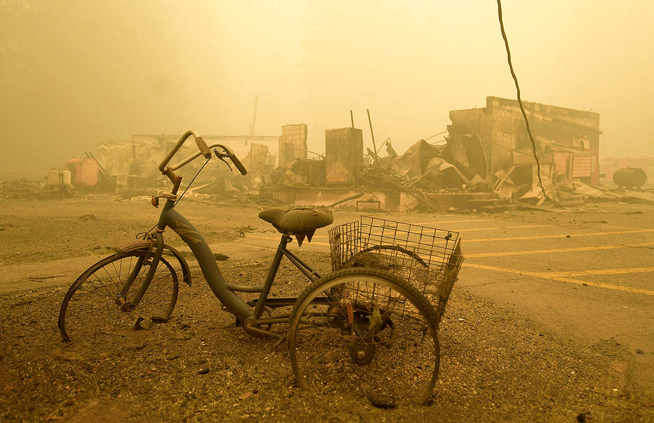 In this Sept. 11, 2020 file photo a trike stands near the burnt remains of a building destroyed by a wildfire near the Lake Detroit Market in Detroit, Ore. The blaze was one of multiple fires that burned across the state last month. Three Pacific Northwest law firms have filed a class action lawsuit against Pacific Power and its parent company, Portland-based PacifiCorp, alleging that the power company failed to shut down its power lines despite a historic wind event and extremely dangerous wildfire conditions. (Mark Ylen/Albany Democrat-Herald via AP, File)