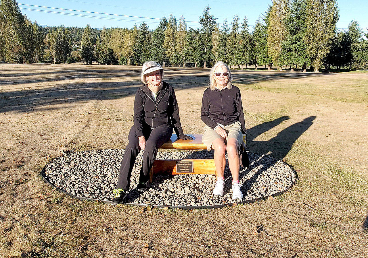 Dee Sweeney, left, captain at Discovery Bay Women’s Golf Club, and Katherine Buchanan, captain at Port Townsend Women’s Golf Club, sit on the newly installed memorial bench in honor of Naomi and Janie Marcus at Port Townsend Golf Course.