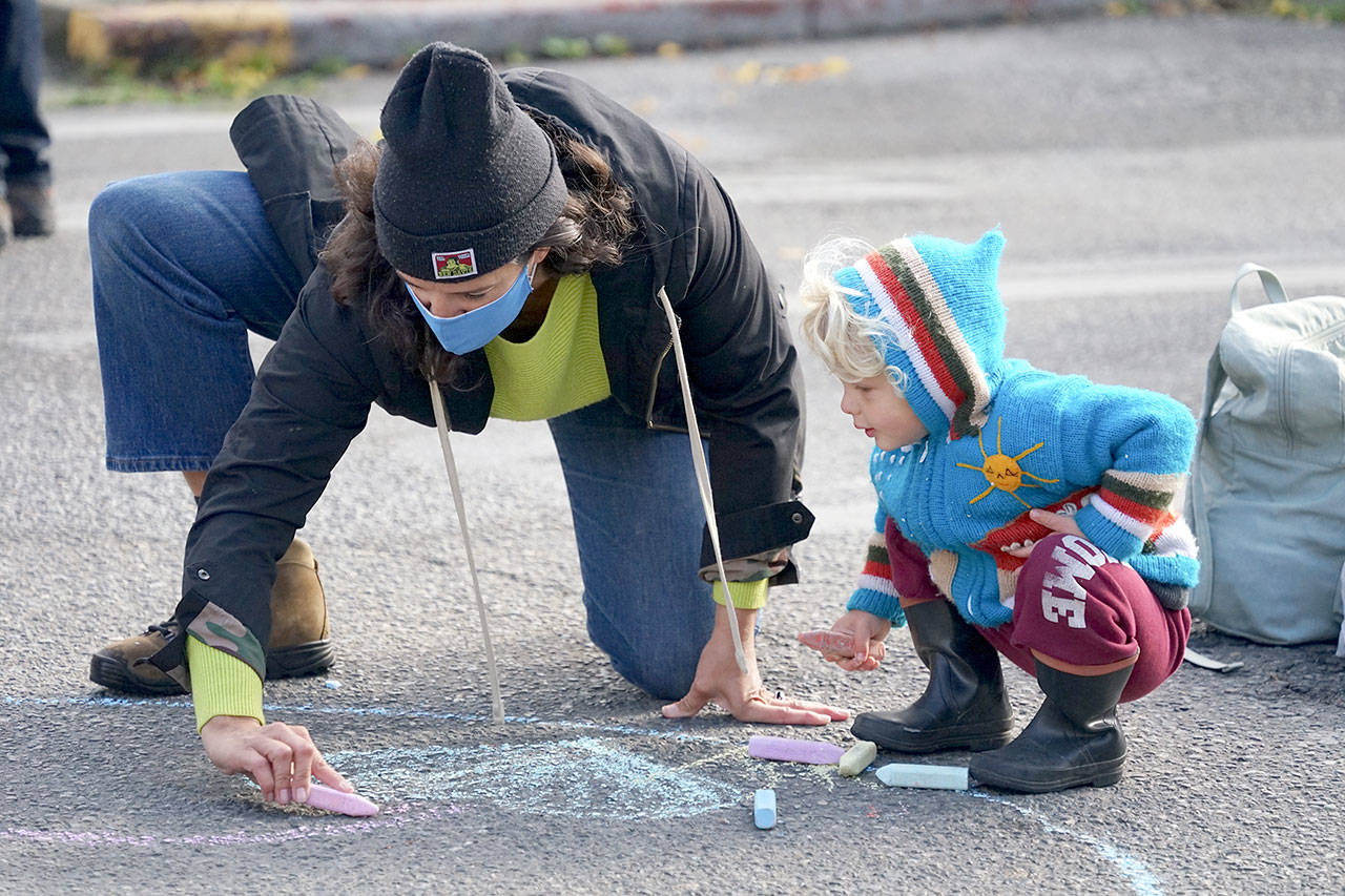 Holly Jarnagin, left, and 2-year-old Frankie Rezendes of Port Townsend make chalk art in the intersection of Lawrence and Tyler streets Saturday during the farmers market in uptown Port Townsend. City staff set up a booth and distributed chalk during Saturday’s market, encouraging people to draw their hopes and dreams for the city’s future. (Nicholas Johnson/Peninsula Daily News)