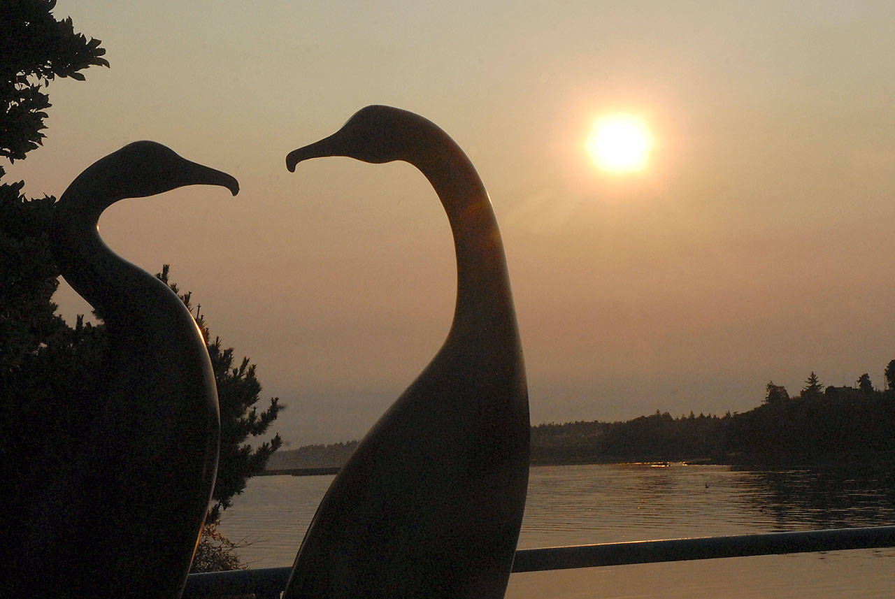 The sculpture “Cormorants” by Port Angeles artist Duncan Yves McKiernan is silhouetted by a smoke-filtered sunrise over Port Angeles Harbor at Port Angeles City Pier in September. (Keith Thorpe/Peninsula Daily News)