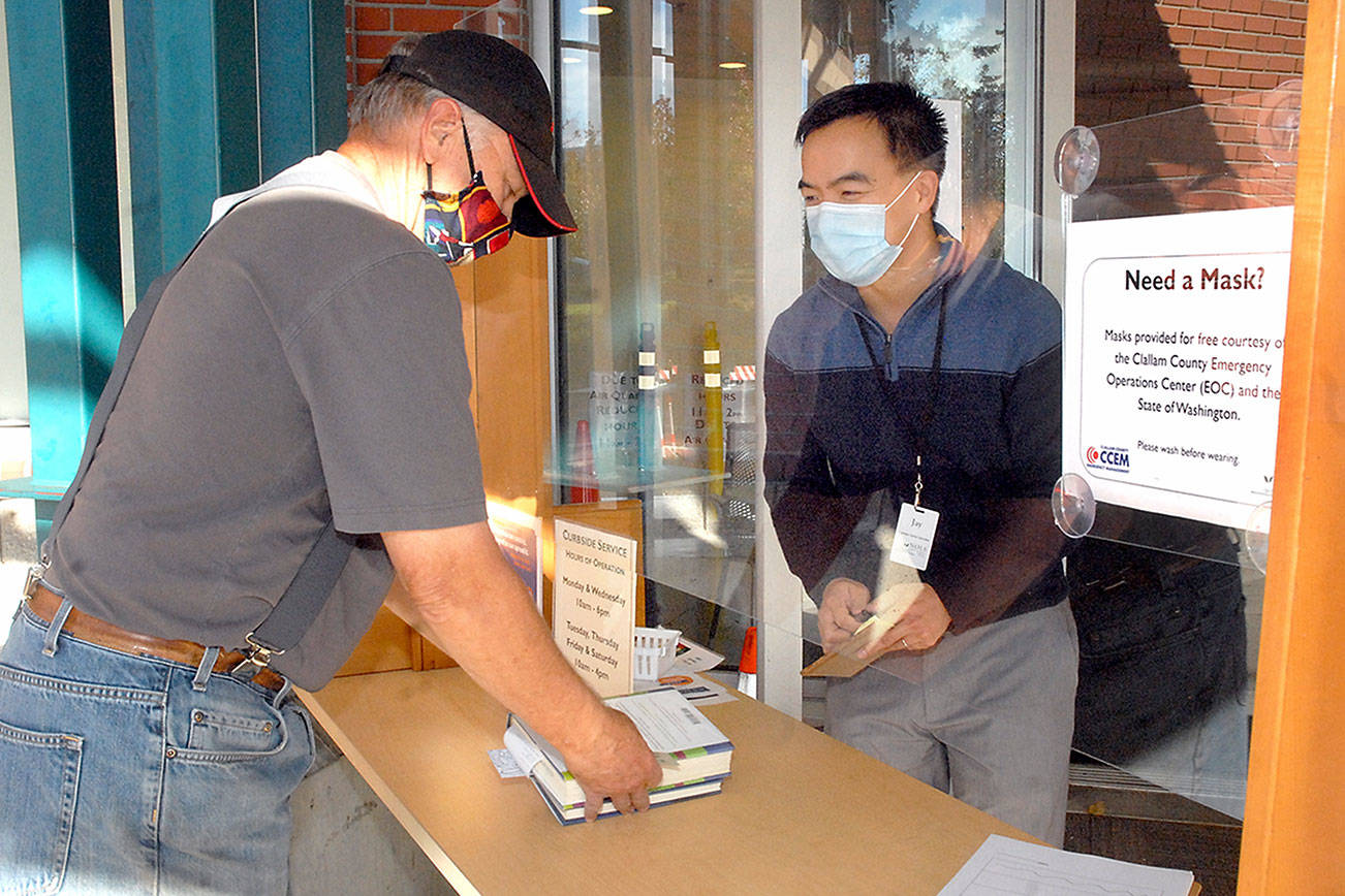 Dan Brooks of Port Angeles, left, checks out books with assistance from customer service representative Jay Averill at the front door of the Port Angeles Public Library on Tuesday. The North Olympic Library System will allow some in-person browsing beginning next month. (Keith Thorpe/Peninsula Daily News)
