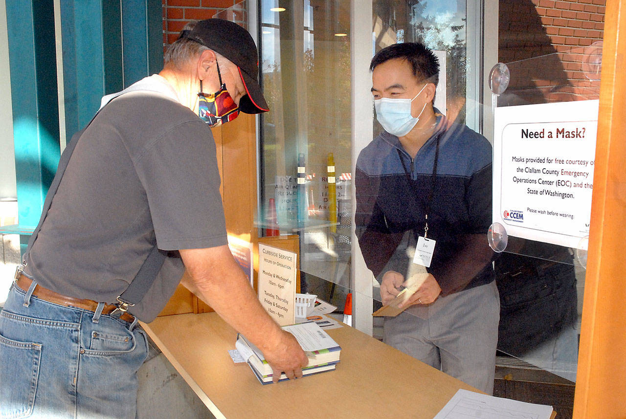 Dan Brooks of Port Angeles, left, checks out books with assistance from customer service representative Jay Averill at the front door of the Port Angeles Public Library on Tuesday, Oct. 20, 2020. The North Olympic Library System will allow some in-person browsing beginning next month. (Keith Thorpe/Peninsula Daily News)